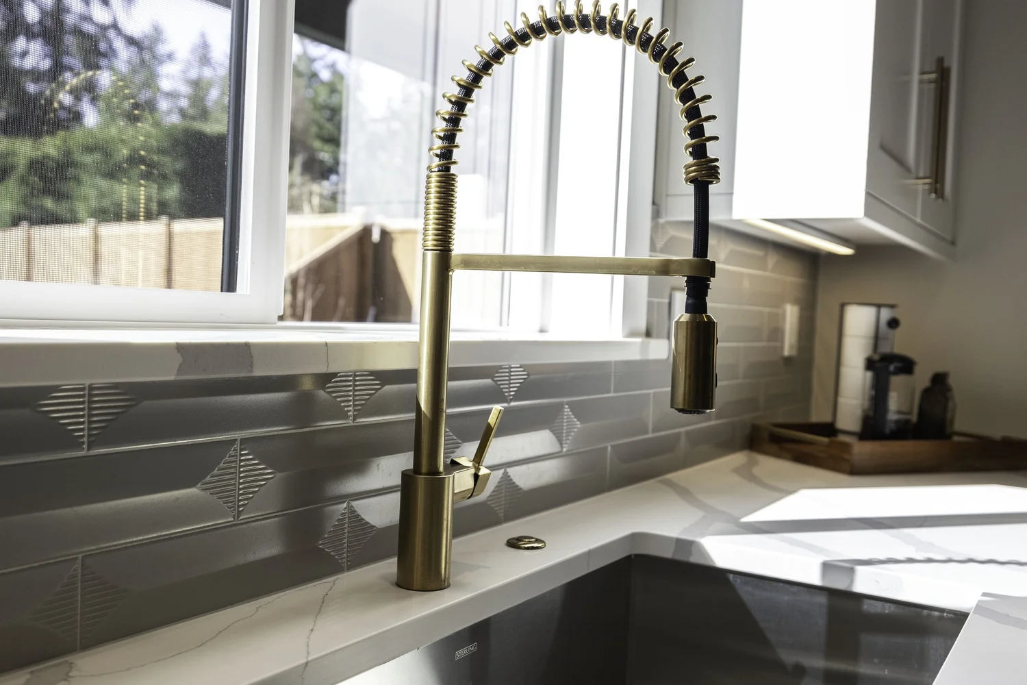 Brass-toned kitchen faucet beside a gray tile backsplash