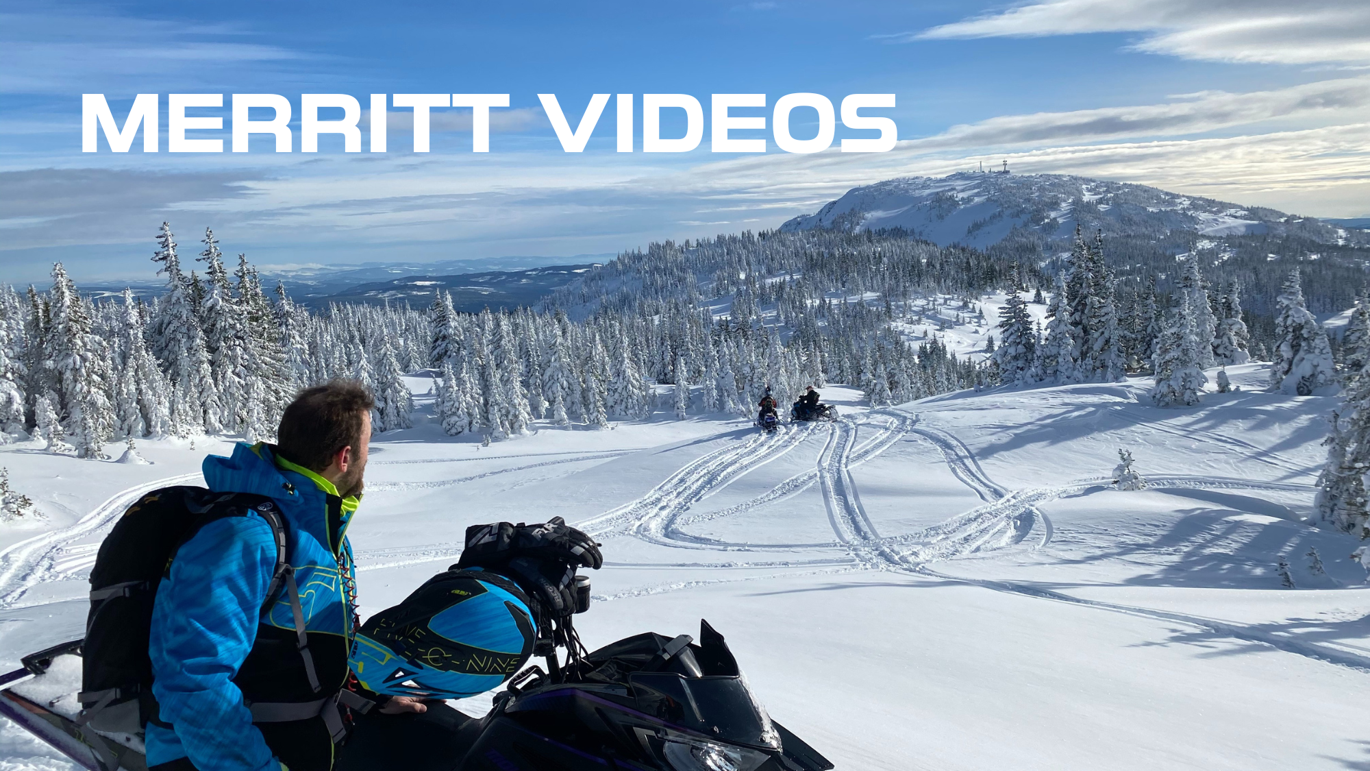 Man in blue jacket and backpack sitting on snowmobile on snowy mountain landscape with pine trees and snowmobiles in the distance, skimming tracks on snow, mountain with radio towers in the background.