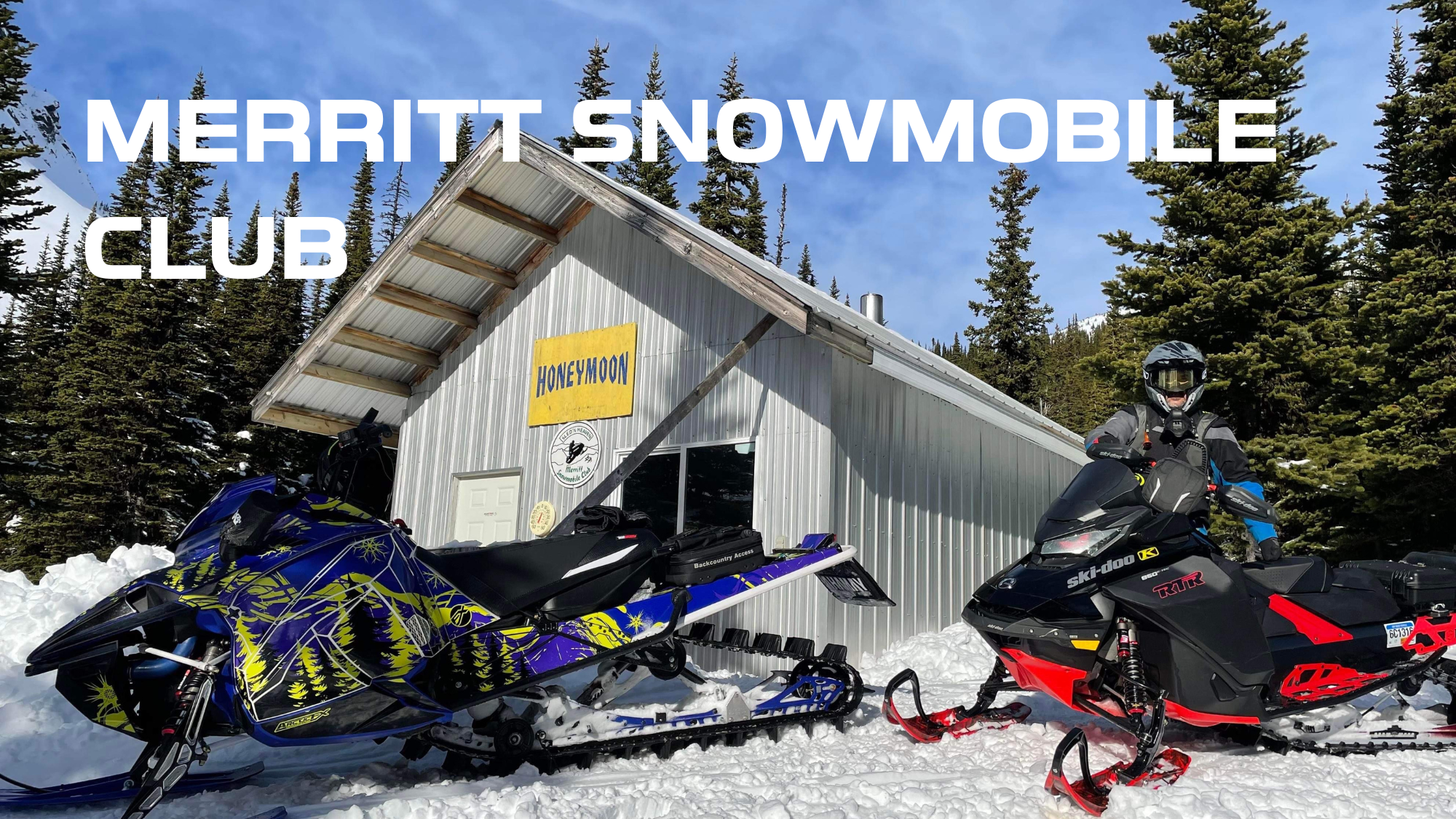 A snowmobile club building with two snowmobiles parked in front, surrounded by snow and evergreen trees on a clear, sunny day.