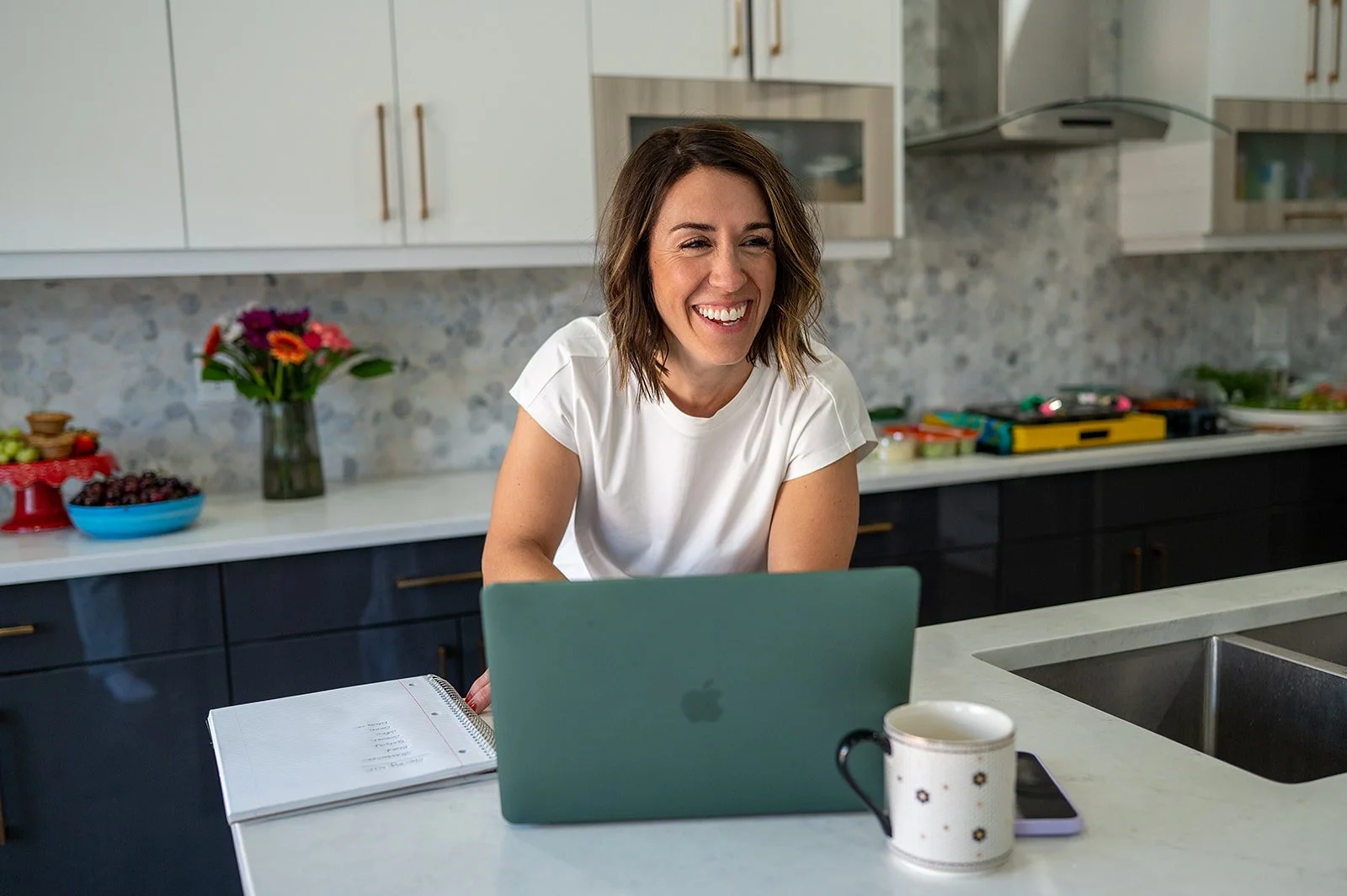 Registered dietitian laughs warmly during a virtual nutrition consultation at her kitchen counter.