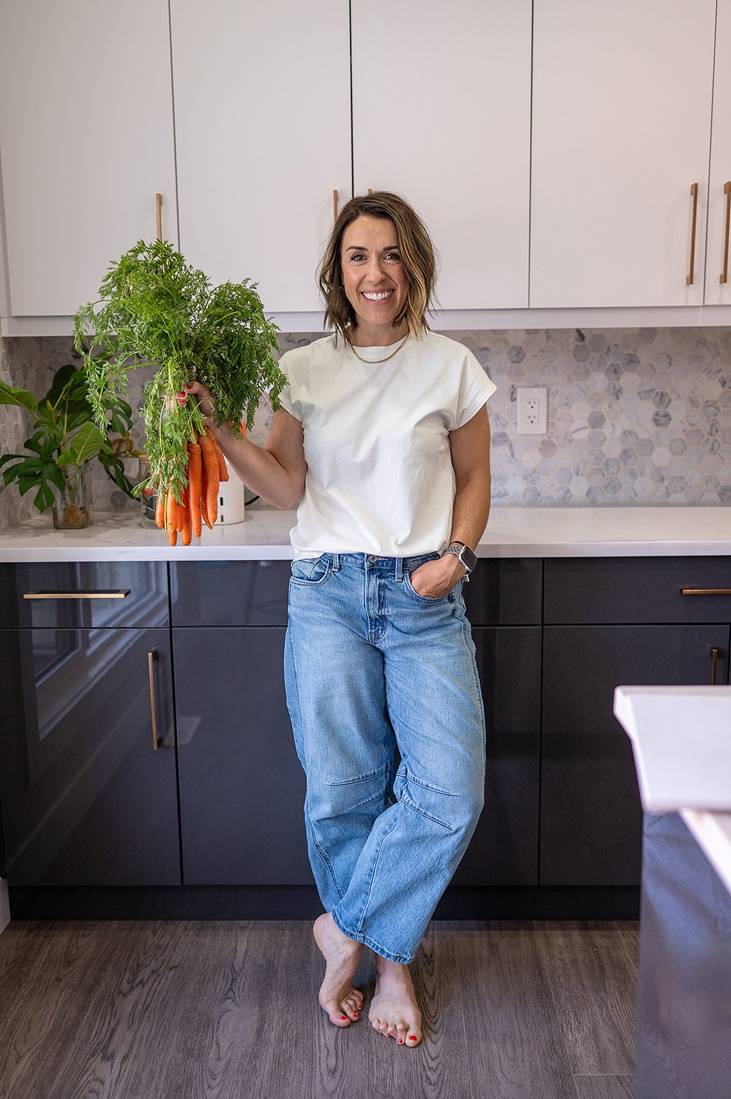 Megan Wallace leaning against a kitchen counter with fresh carrots and a colorful flower bouquet nearby
