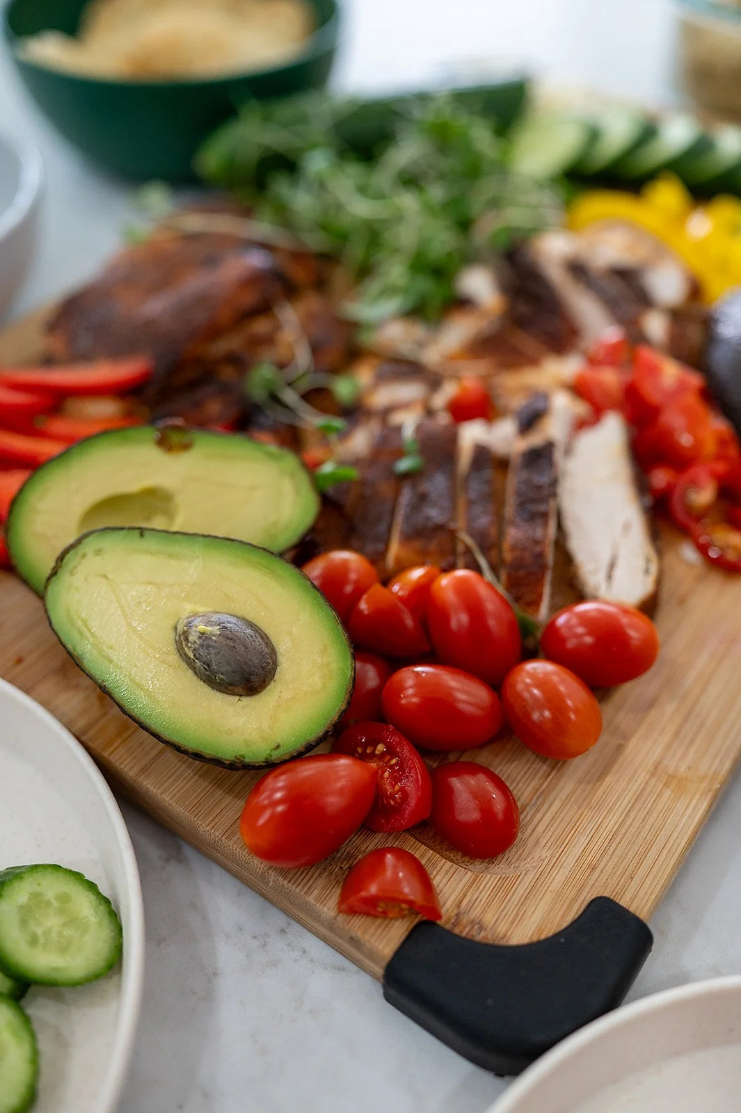 Close-up of halved avocado and cherry tomatoes on a platter with blackened chicken in the background