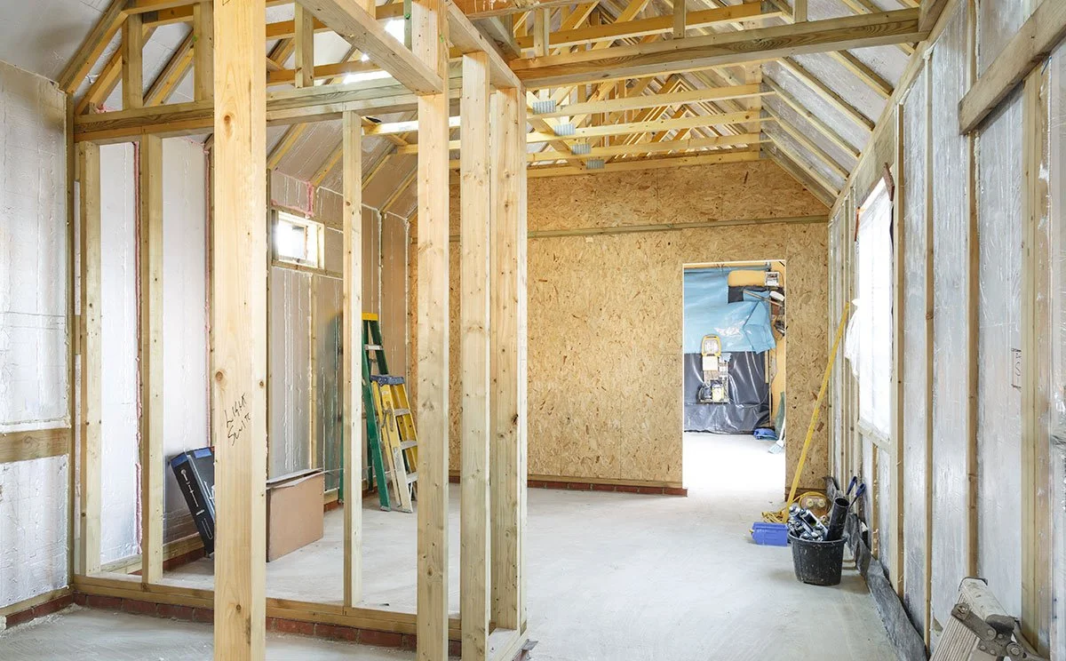 Interior of a house under construction with exposed wooden framing and drywall.