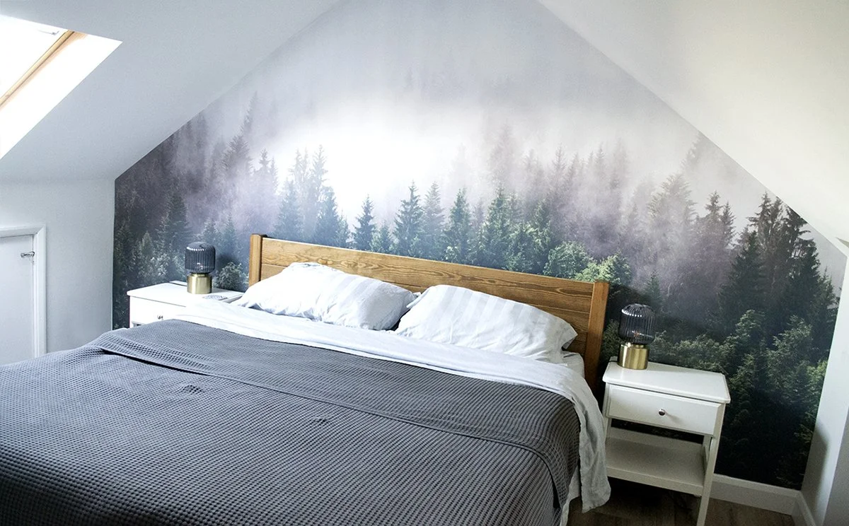 Bedroom with a double bed, white bedside tables with lamps, and a forest mural on the wall behind the bed.