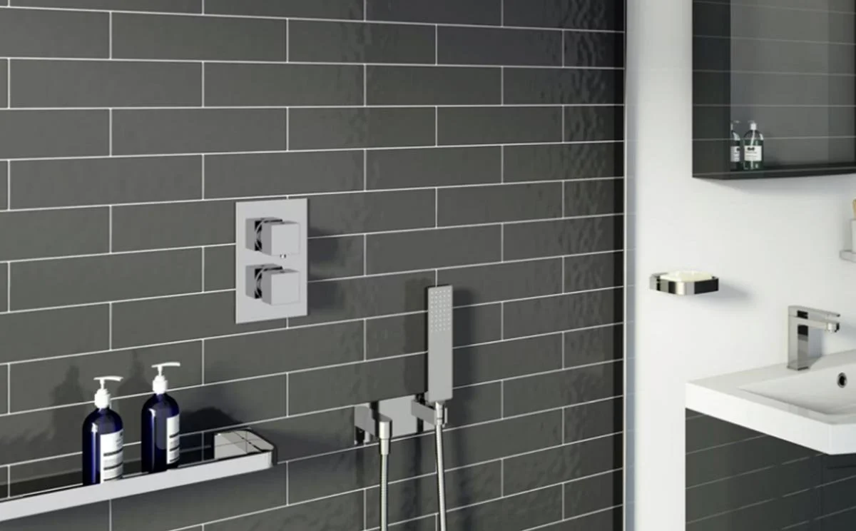 Modern bathroom with a gray tiled wall, shower fixtures, a sink, and toiletries.