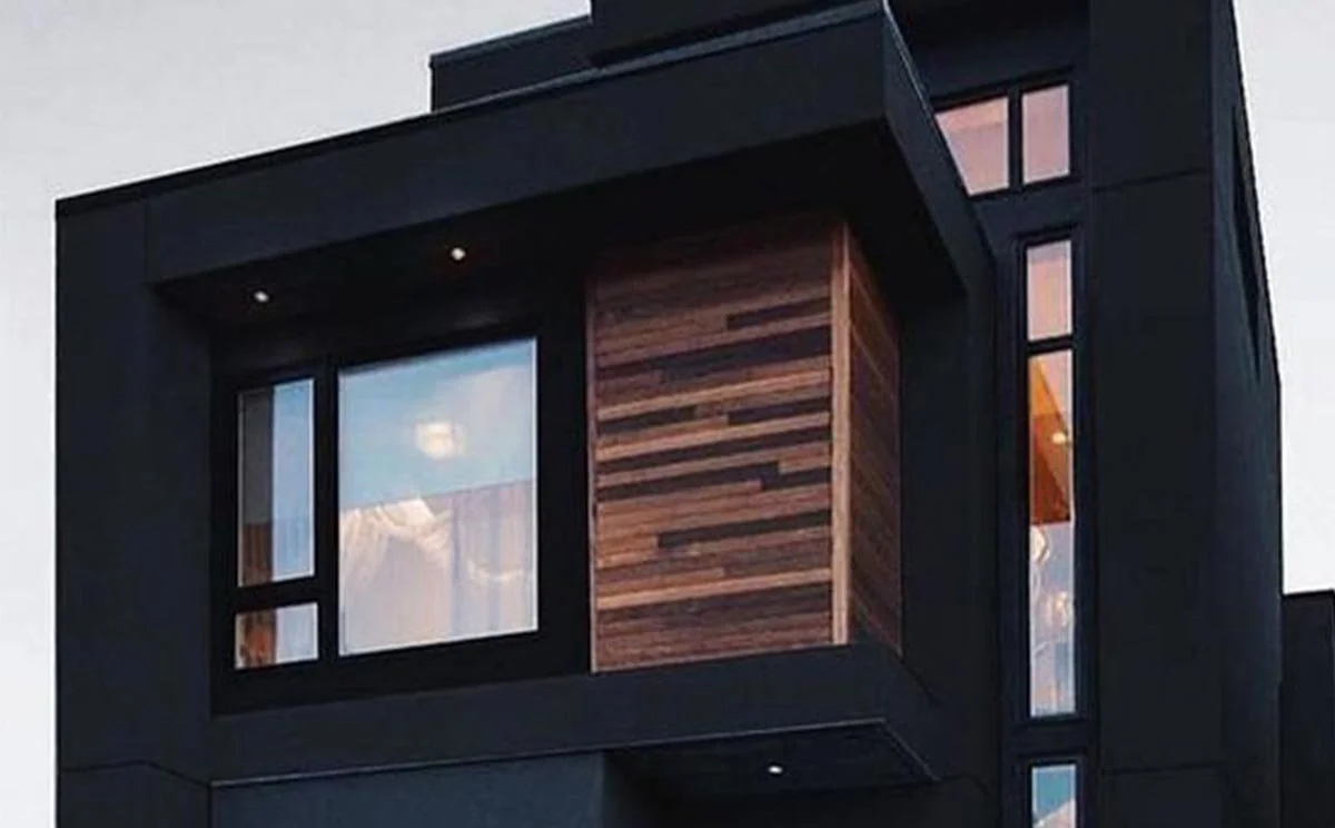 Close-up of a modern building with black exterior walls, wooden accents, and large windows.