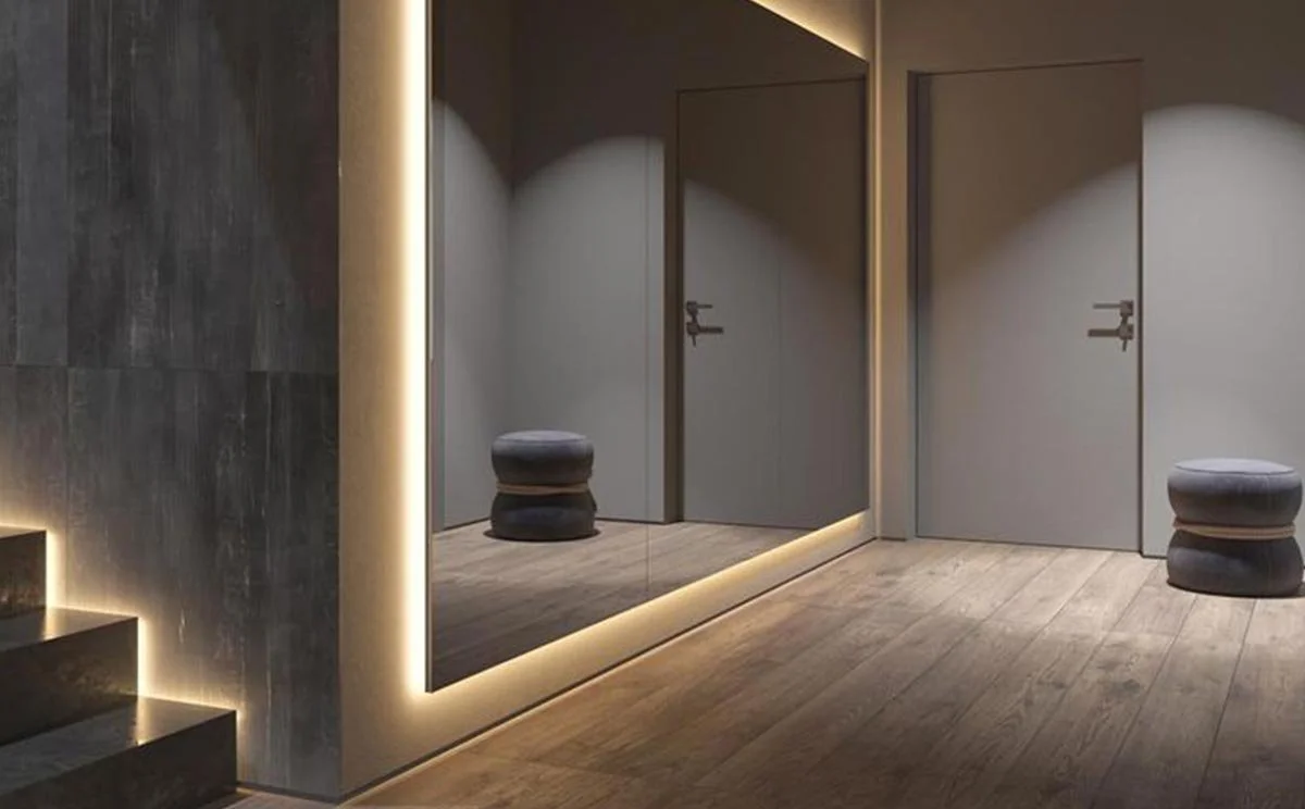 A modern hallway with a large mirror, two gray stools, and two closed doors.