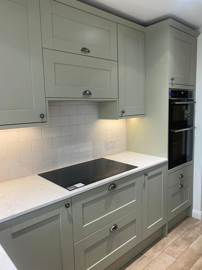 Kitchen with light green cabinets, white tile backsplash, black induction cooktop, and built-in oven.