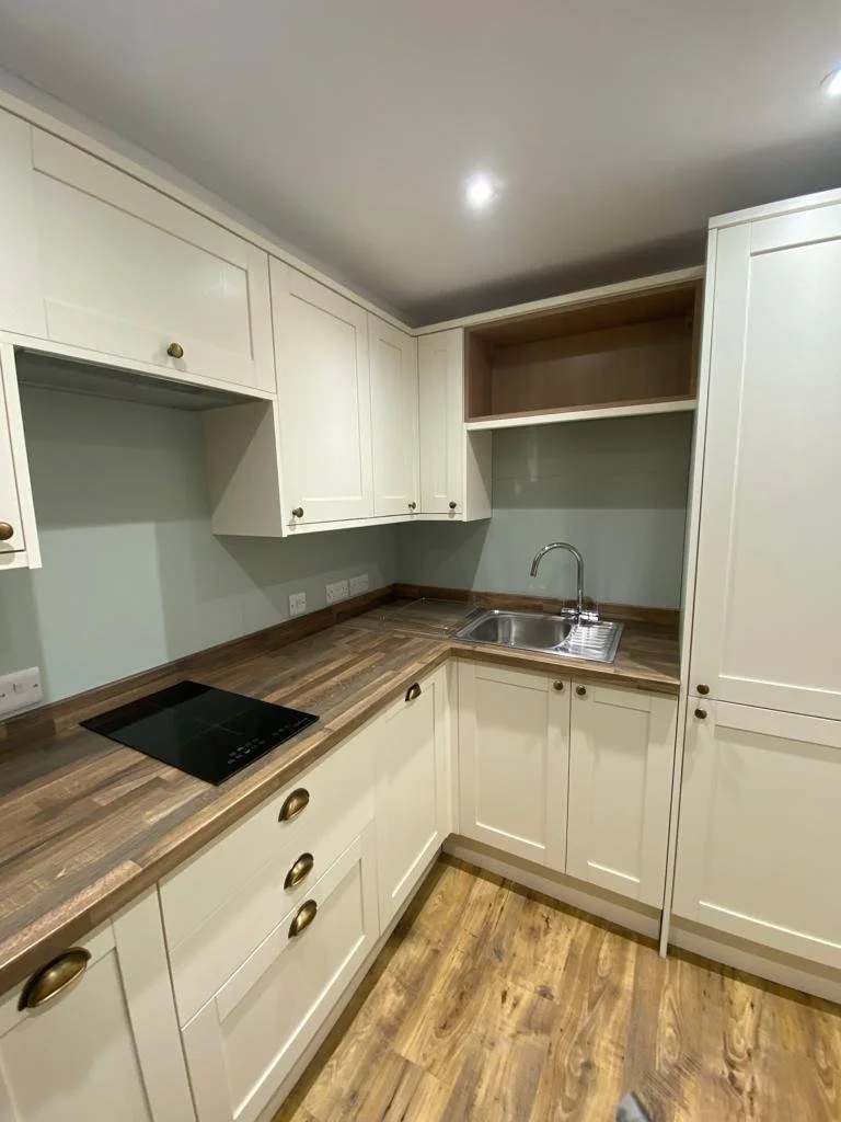 Kitchen with cream-colored cabinets, wooden countertop, sink, open shelving, and electrical outlets.