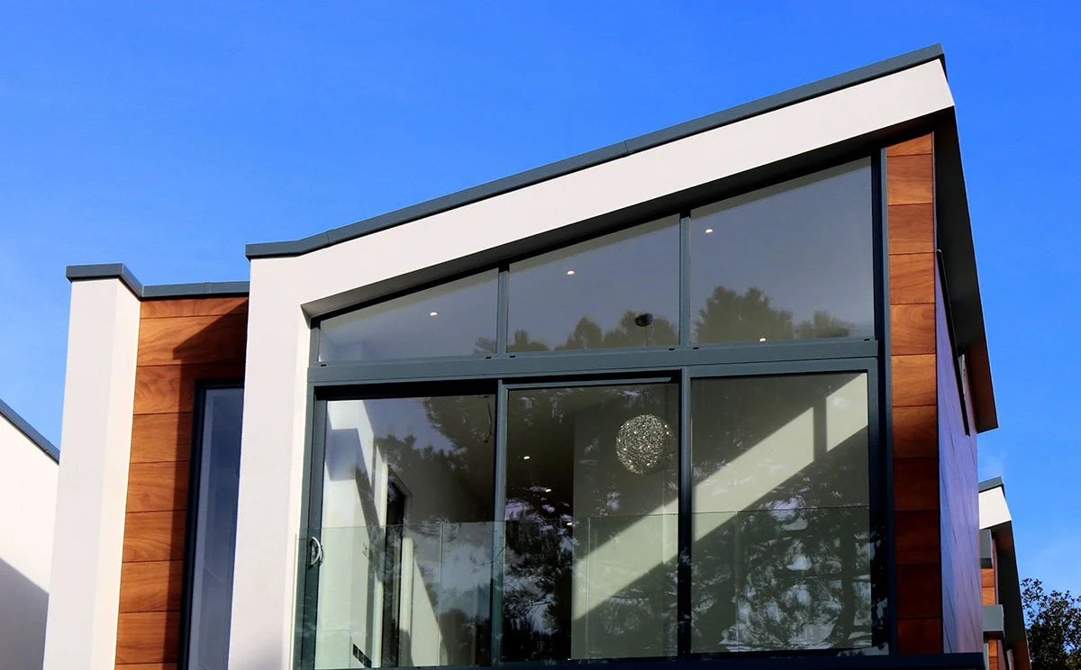 Modern house with large glass windows and wooden panels under a clear blue sky.