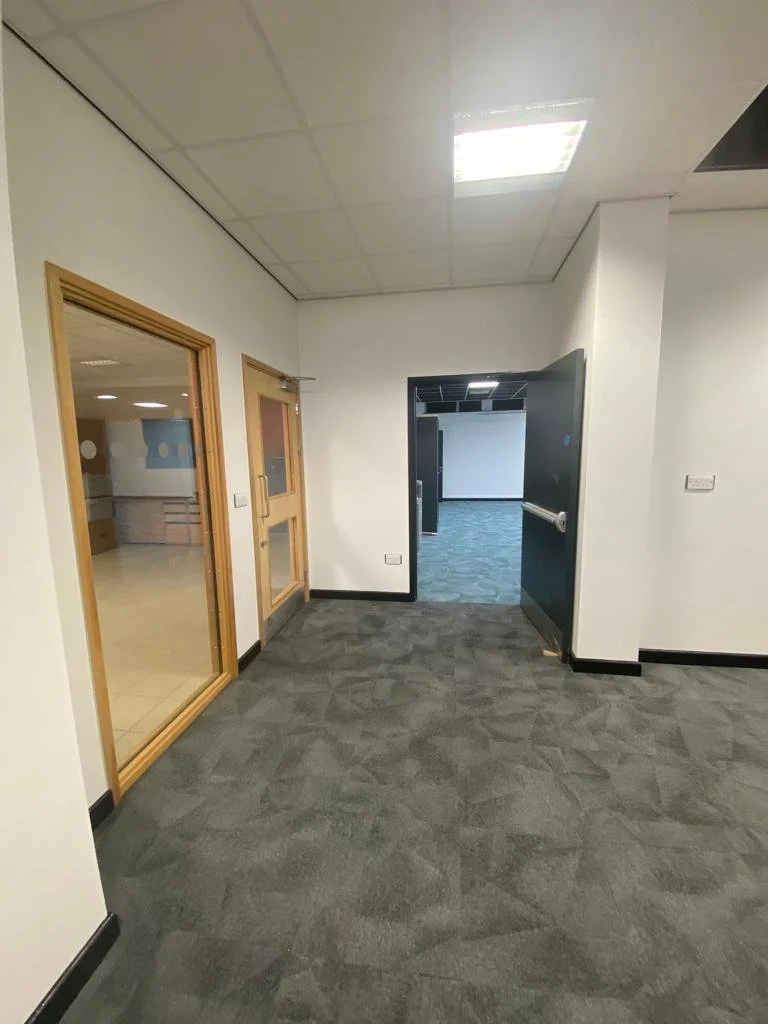 Empty office hallway with grey carpet, white walls, and multiple doors leading to different rooms.