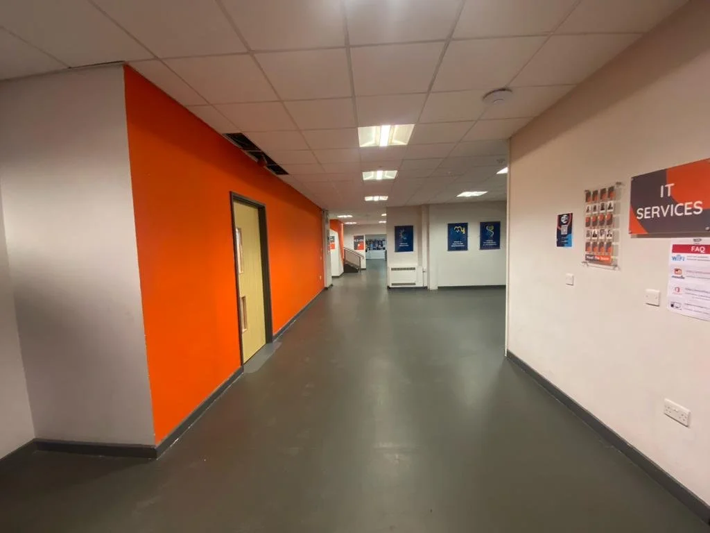 Empty hallway with orange and white walls, and posters on the wall, in an indoor building.