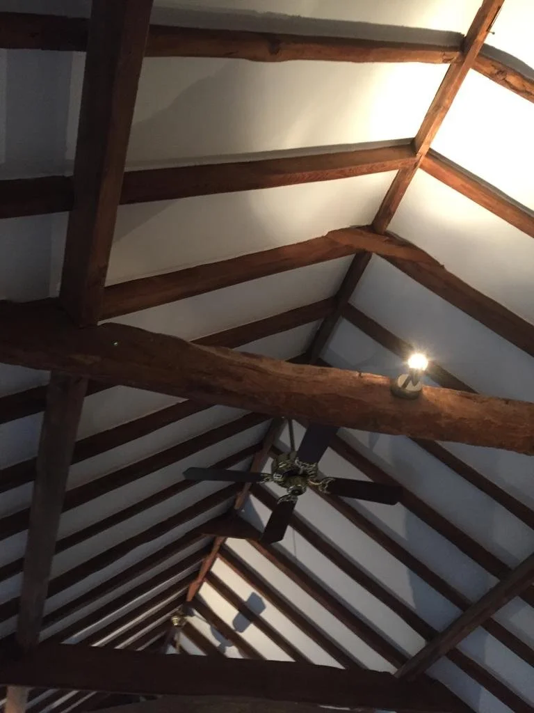 Interior view of a vaulted ceiling with wooden beams and a ceiling fan.