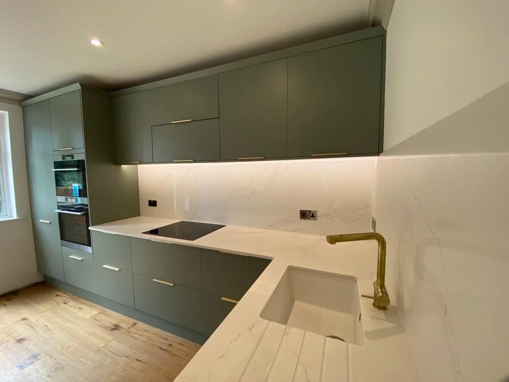 Modern kitchen with green cabinets, a white marble countertop and backsplash, a black induction cooktop, and a gold faucet over the sink.