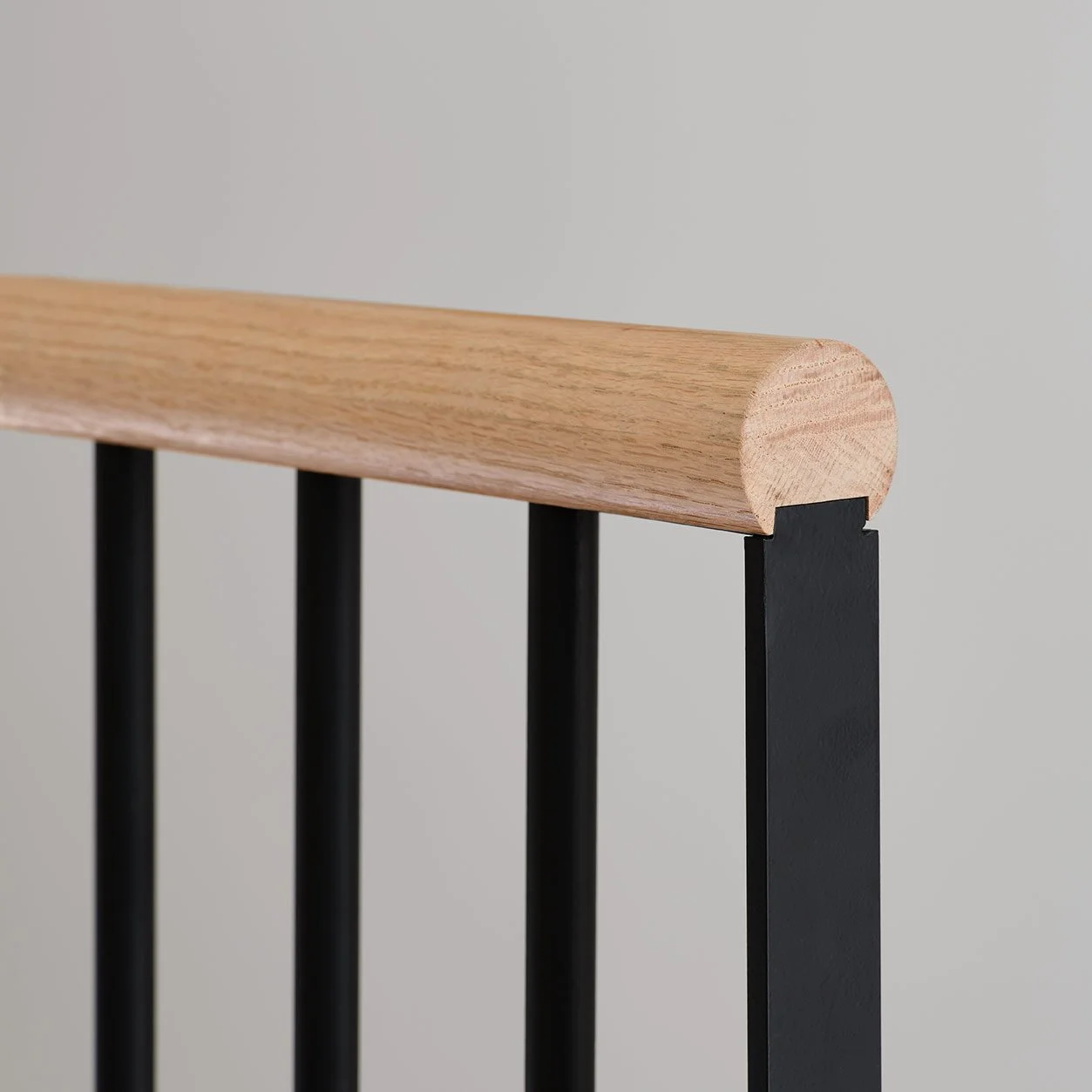 Close-up of a modern chair backrest with a wooden top rail and black metal vertical supports.