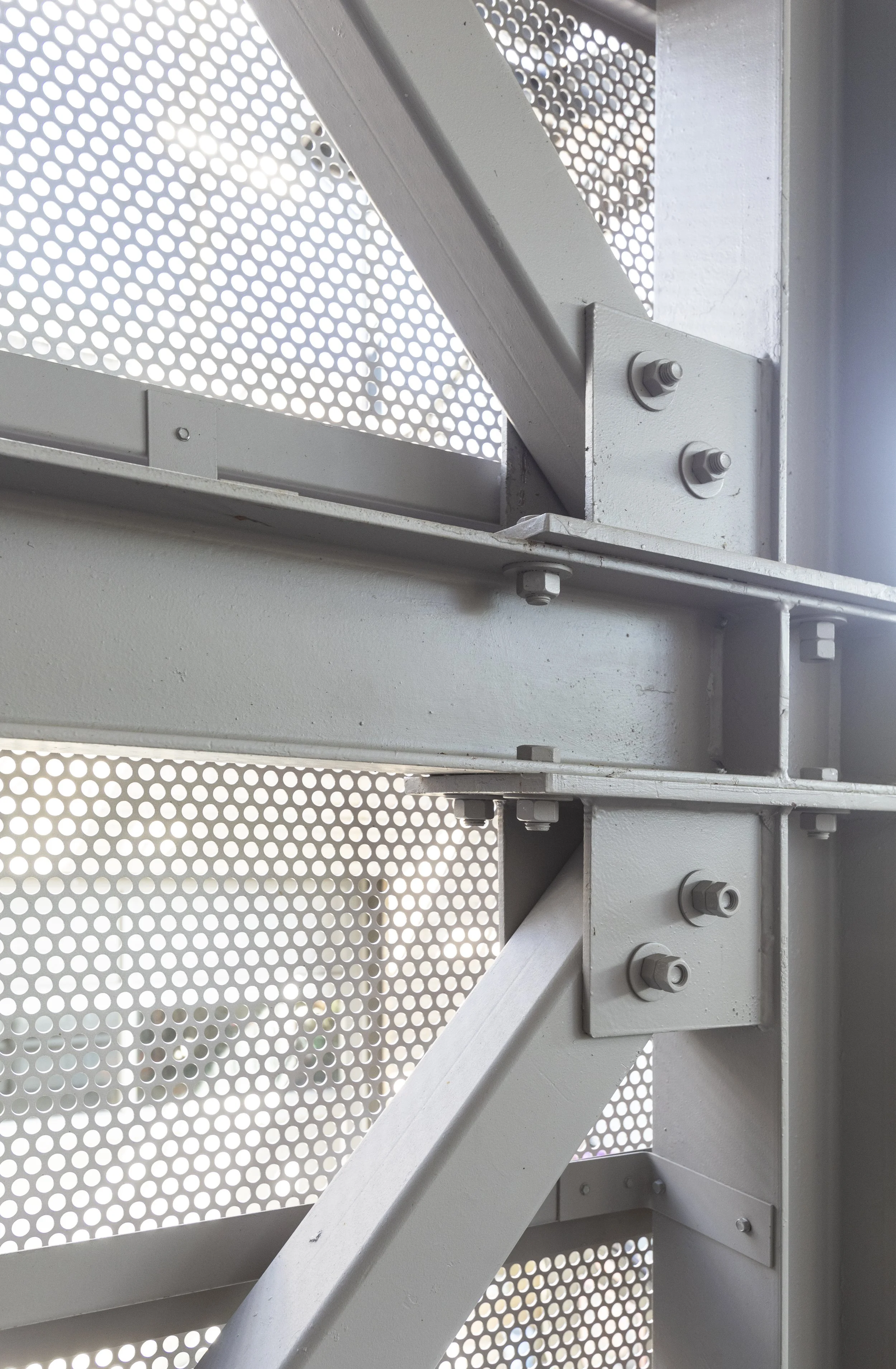 Close-up of a metallic structure with bolts and perforated panels, possibly part of an industrial or architectural framework.