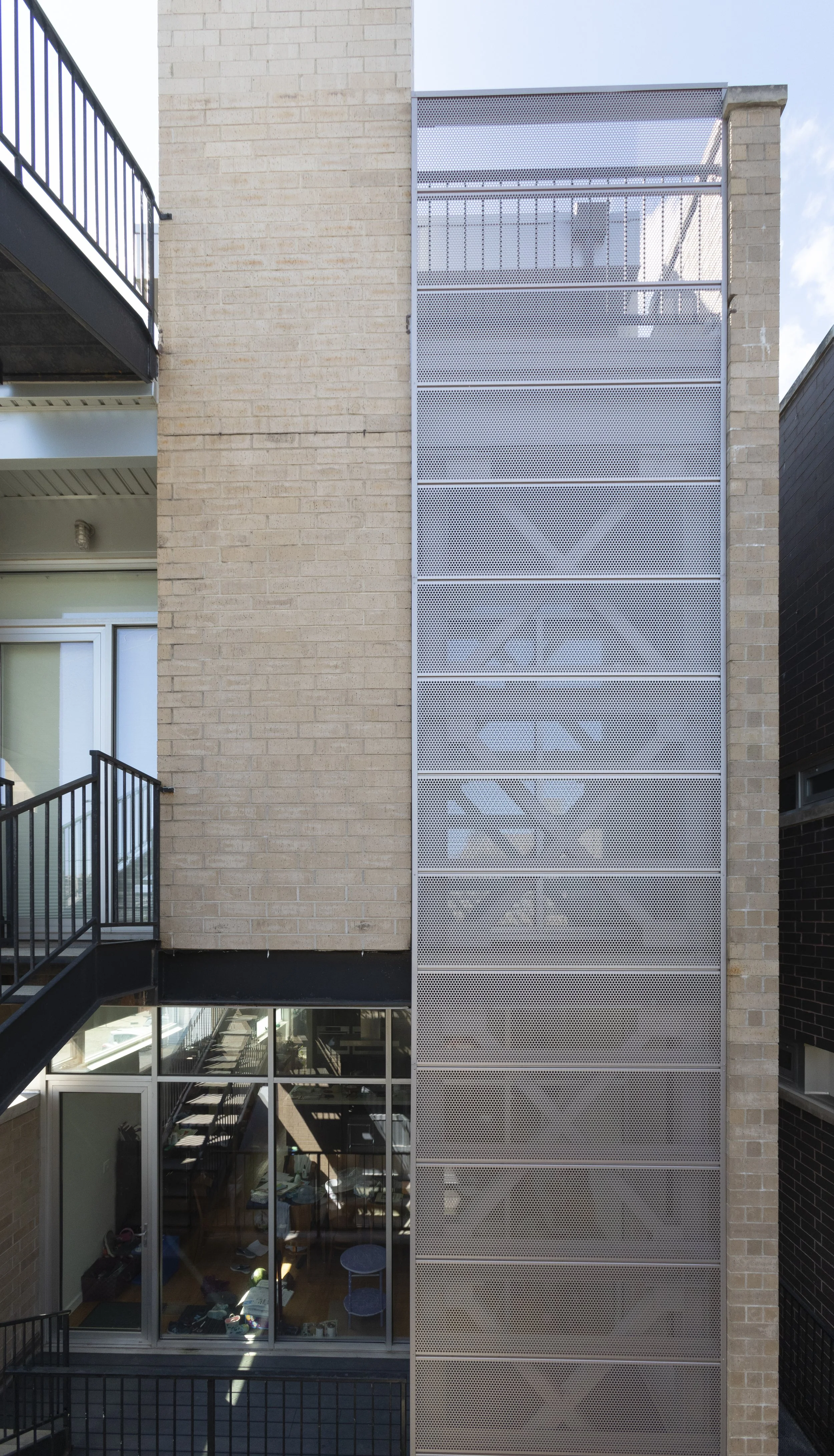 Photo of a modern apartment building's exterior with a brick wall, glass doors and windows, and a metal balcony with railings.