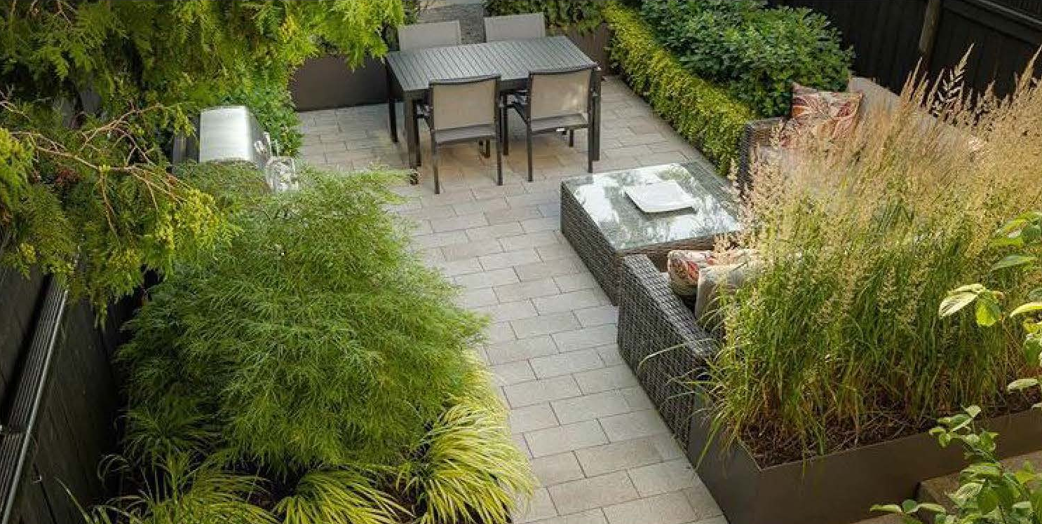 Animal care employee sanctuary. Aerial view of a landscaped courtyard with a metal dining table and chairs, a wicker lounge set, dense ornamental grasses and shrubs, enclosed by a privacy fence.