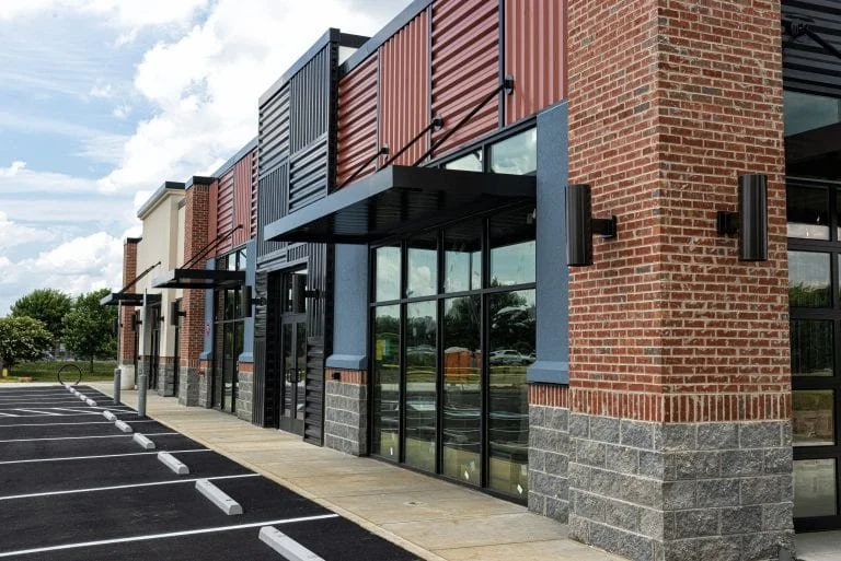 Exterior view of a modern commercial building with brick, metal siding, large glass windows, and parking spaces in front.