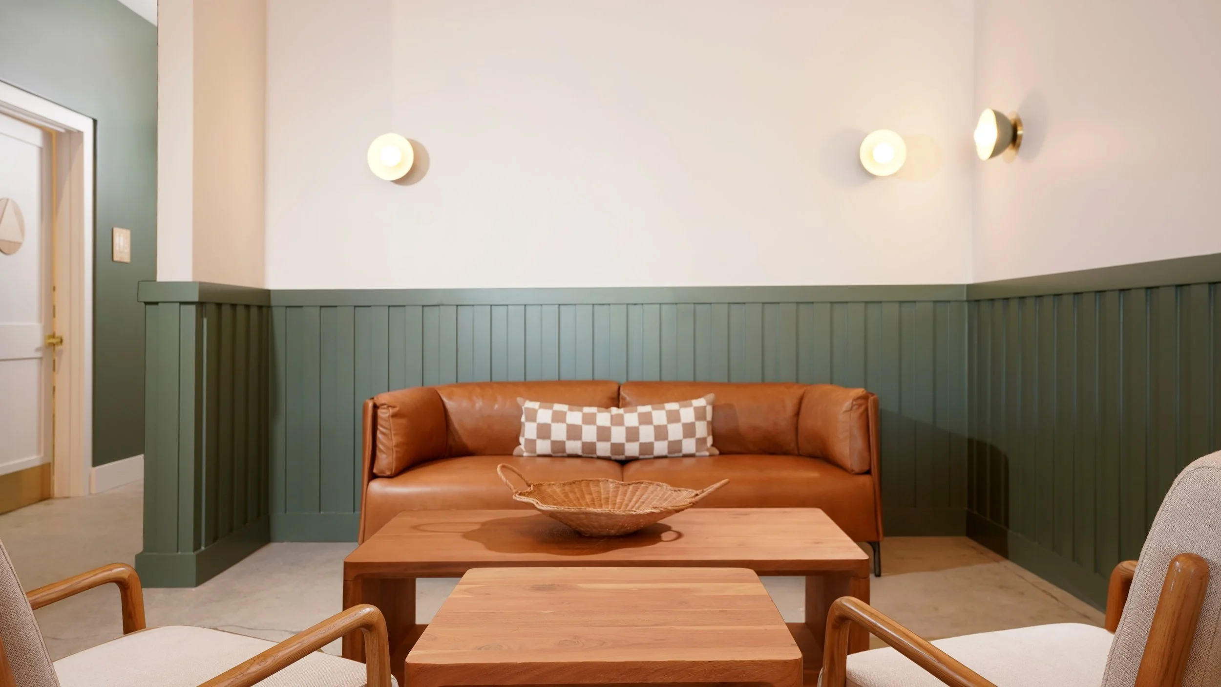 Finished coffee shop lounge with built-in leather bench seating, green wainscoting, light wood tables, and modern minimalist chairs.