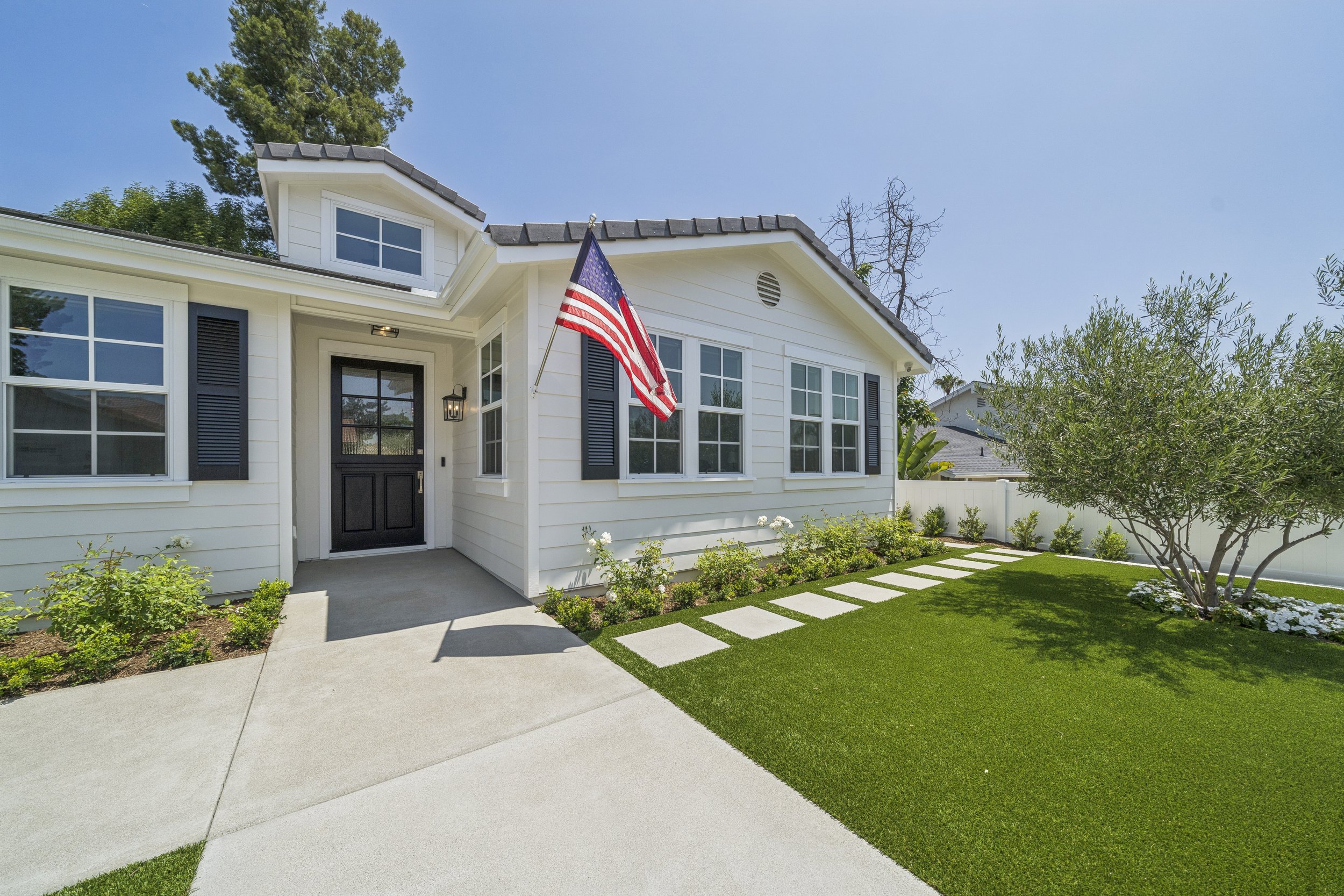 Exterior view of a Mission Viejo custom home remodel with white siding, black shutters, black front door, concrete walkway, green lawn, and updated landscaping.