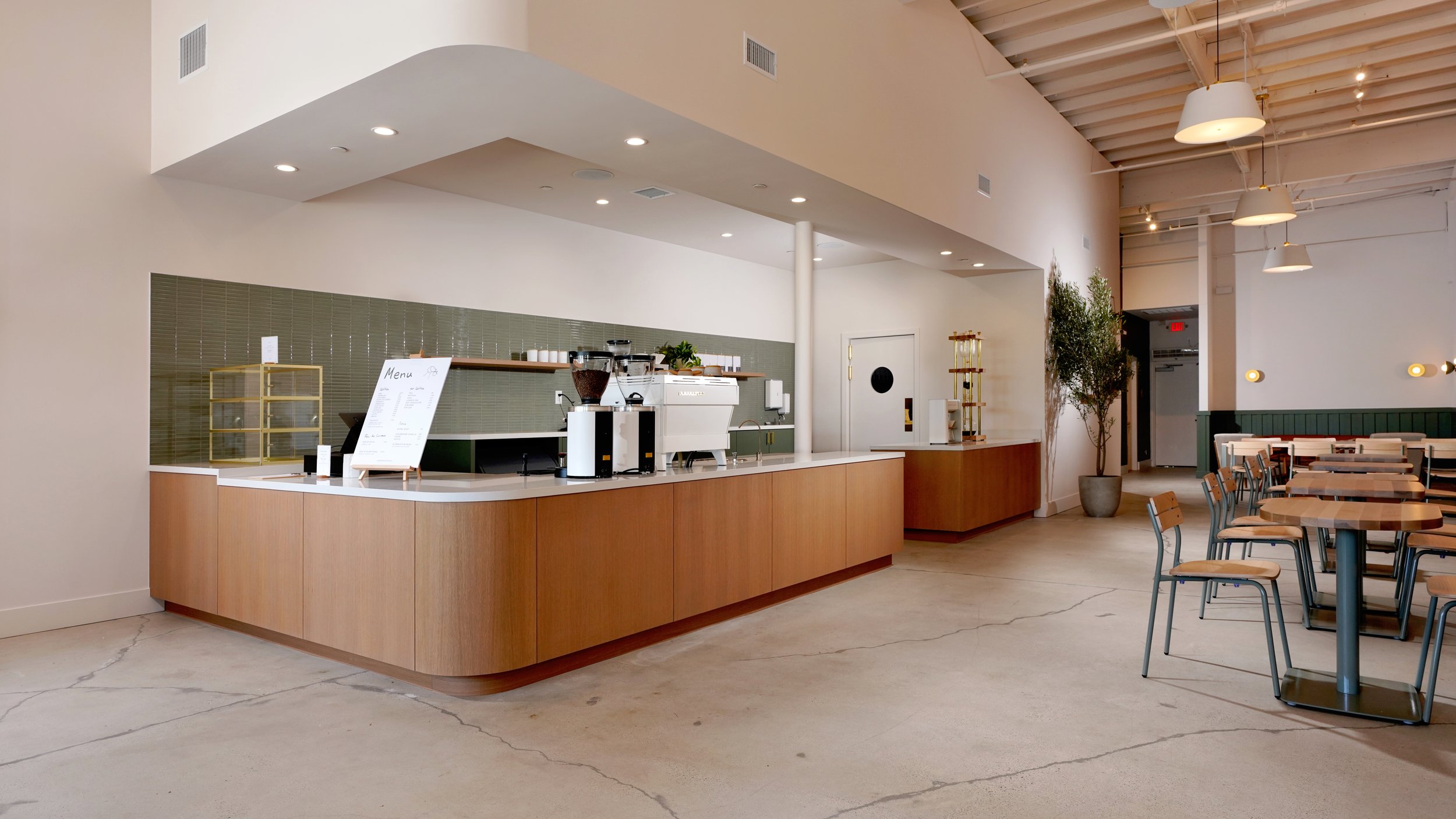 Coffee shop service area with custom wood cabinetry, built-in beverage cooler, black window trim, and clean modern finishes.
