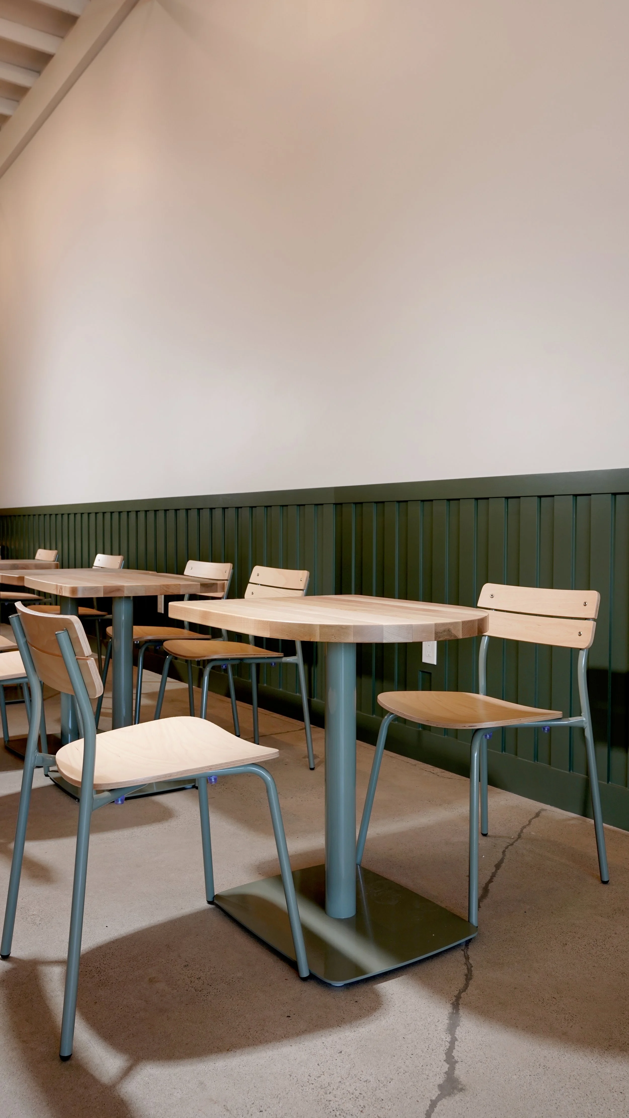 Coffee shop dining area with wood tables, green banquette wall detail, and polished concrete flooring in Laguna Hills, Orange County.