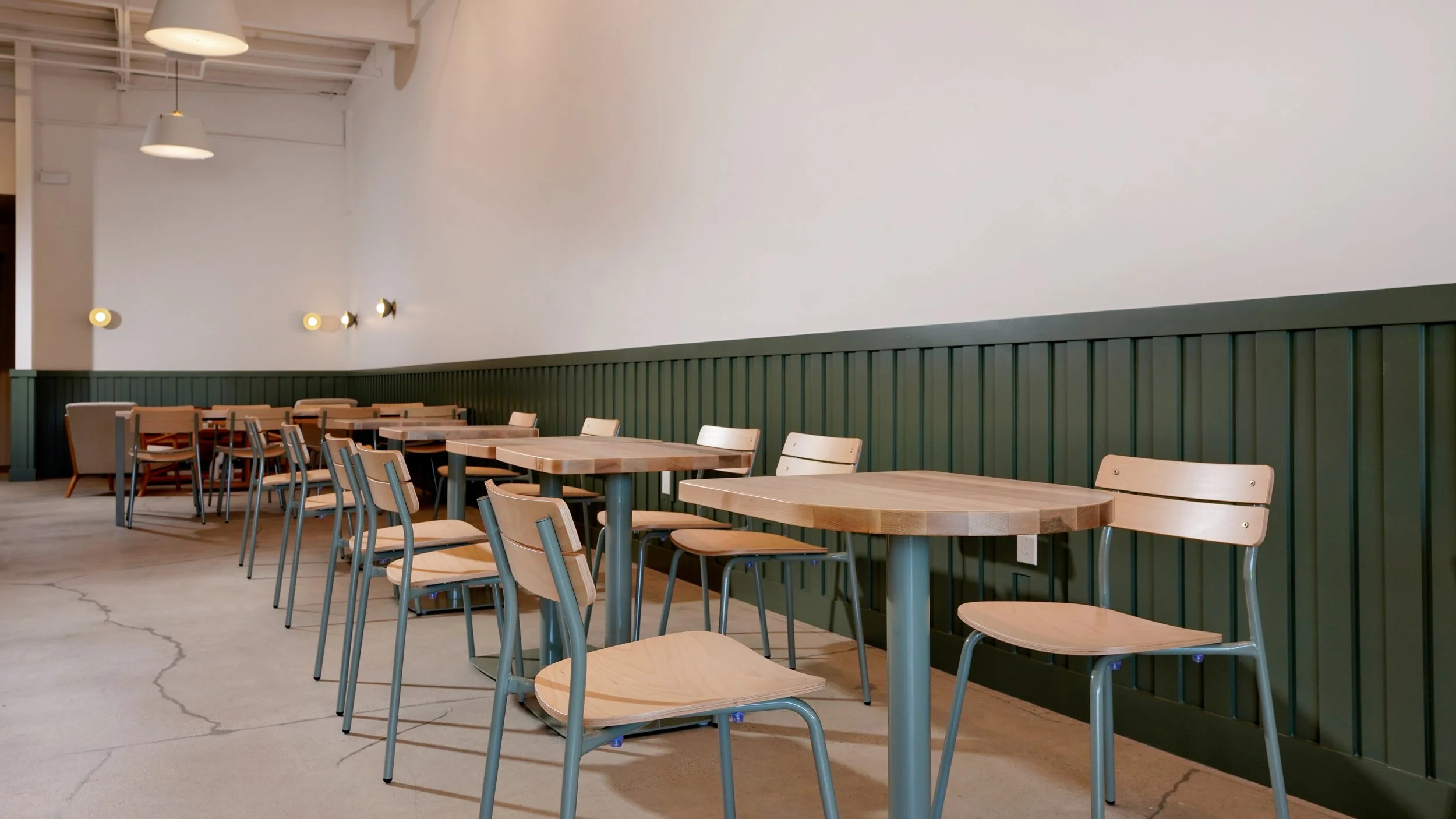 Finished coffee shop dining area with a row of tables, green wainscoting, polished floors, and clean modern lighting.