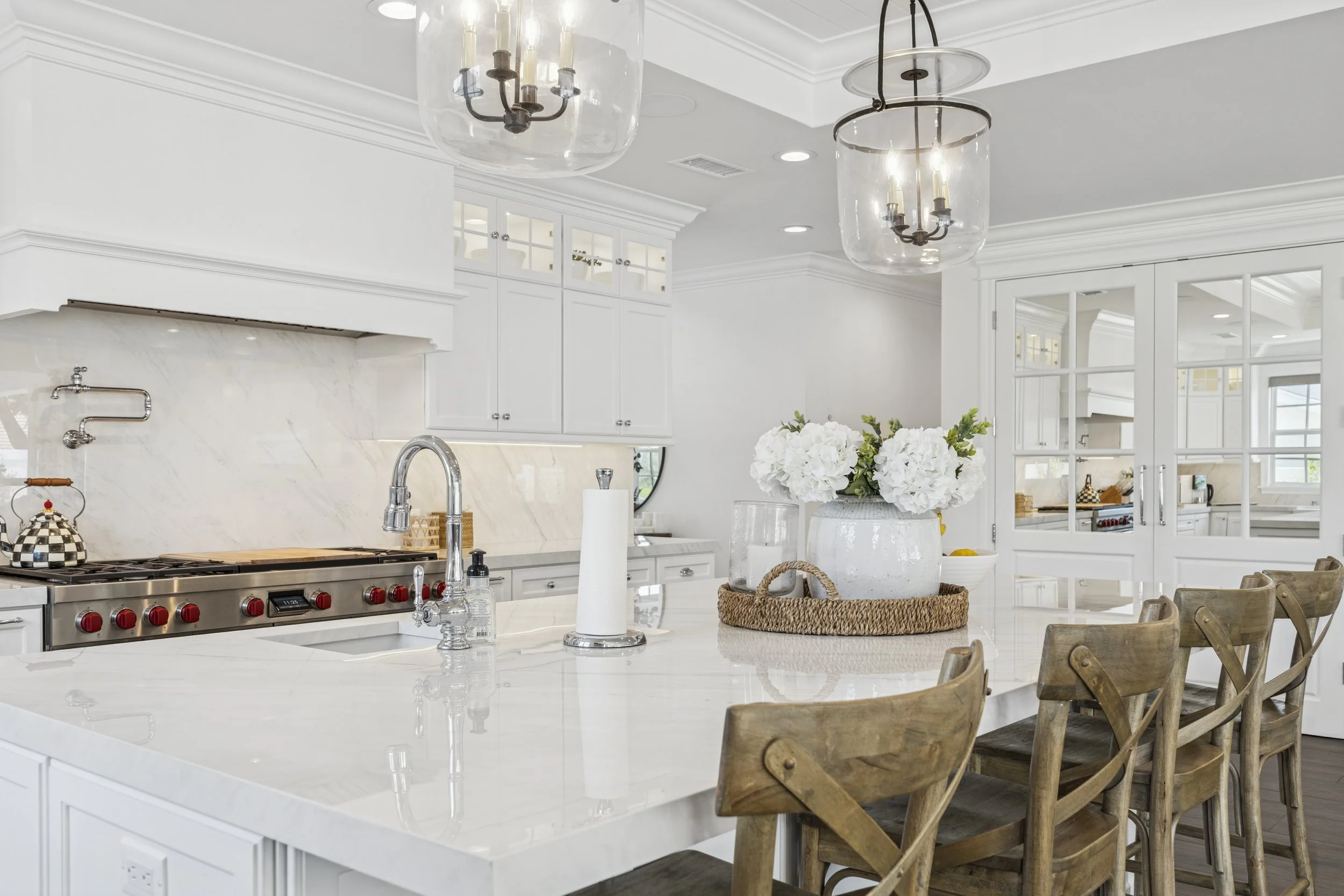 Open-concept kitchen and living room in a Mission Viejo custom home with white cabinetry, large island, pendant lights, wood flooring, fireplace, and backyard views.