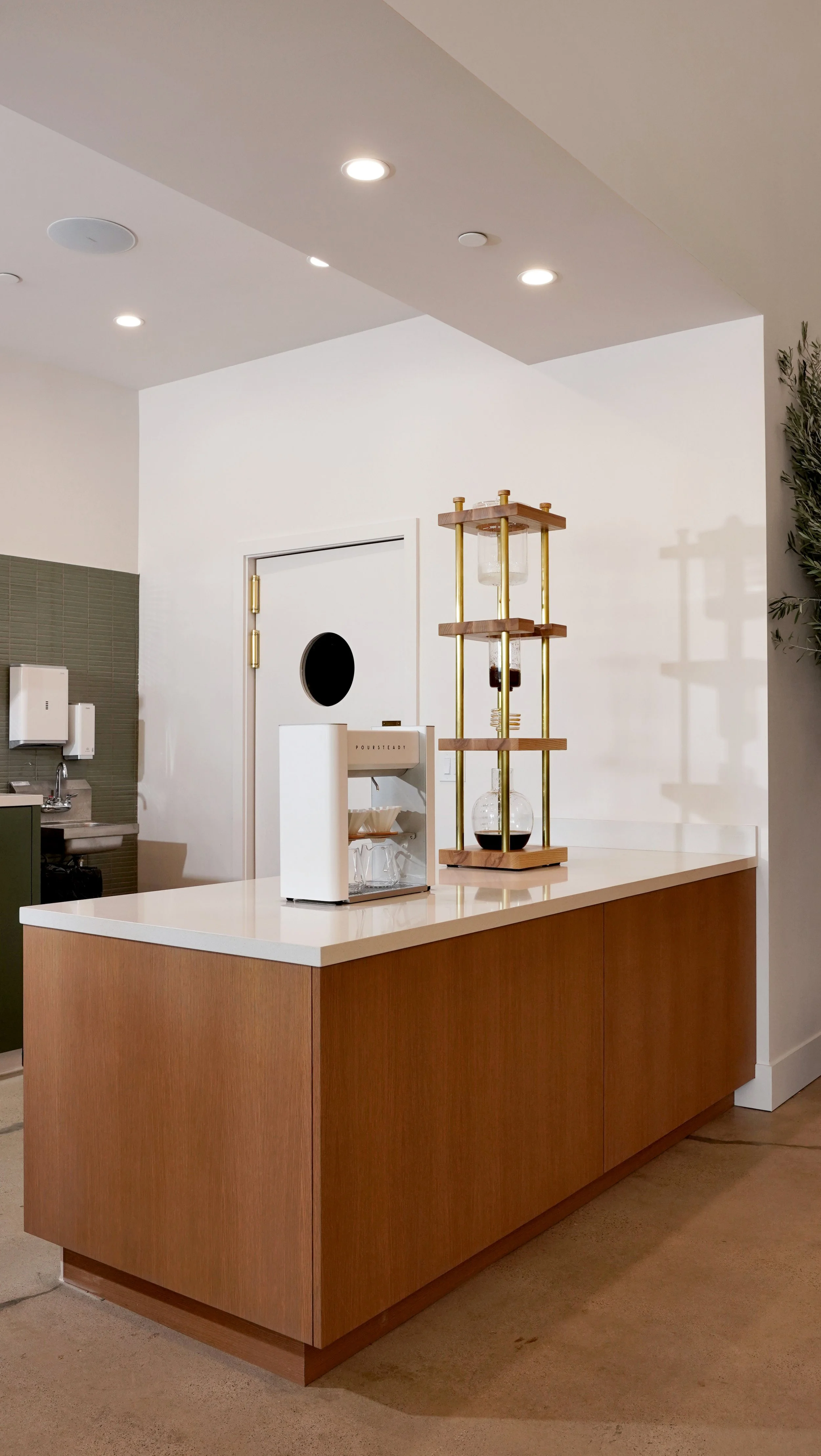 Coffee shop service counter with custom wood cabinetry, open shelving, white countertop, and clean modern commercial finishes.