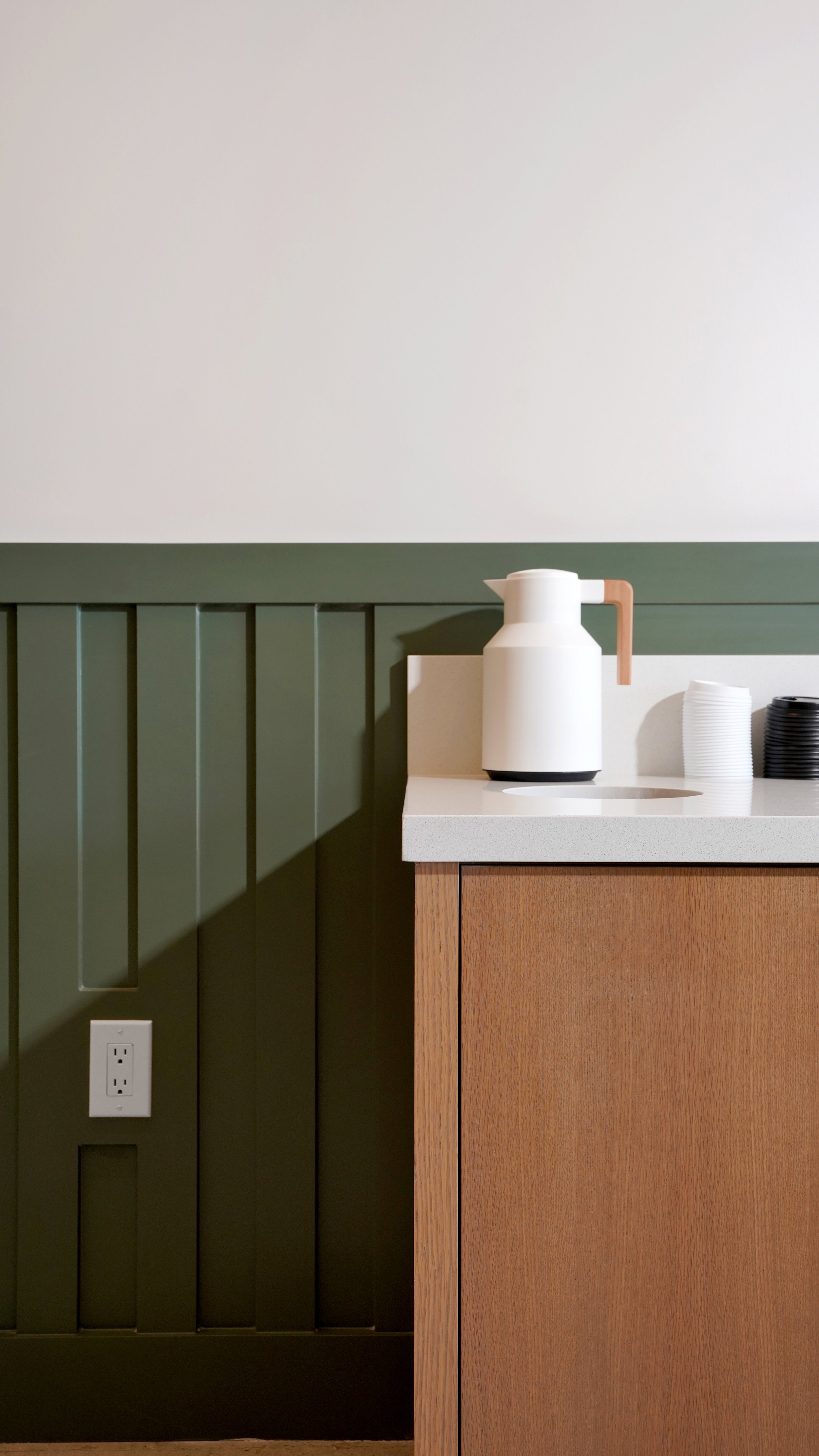 Coffee shop detail with green paneled wall, wood counter, white espresso cups, and clean commercial finish work.