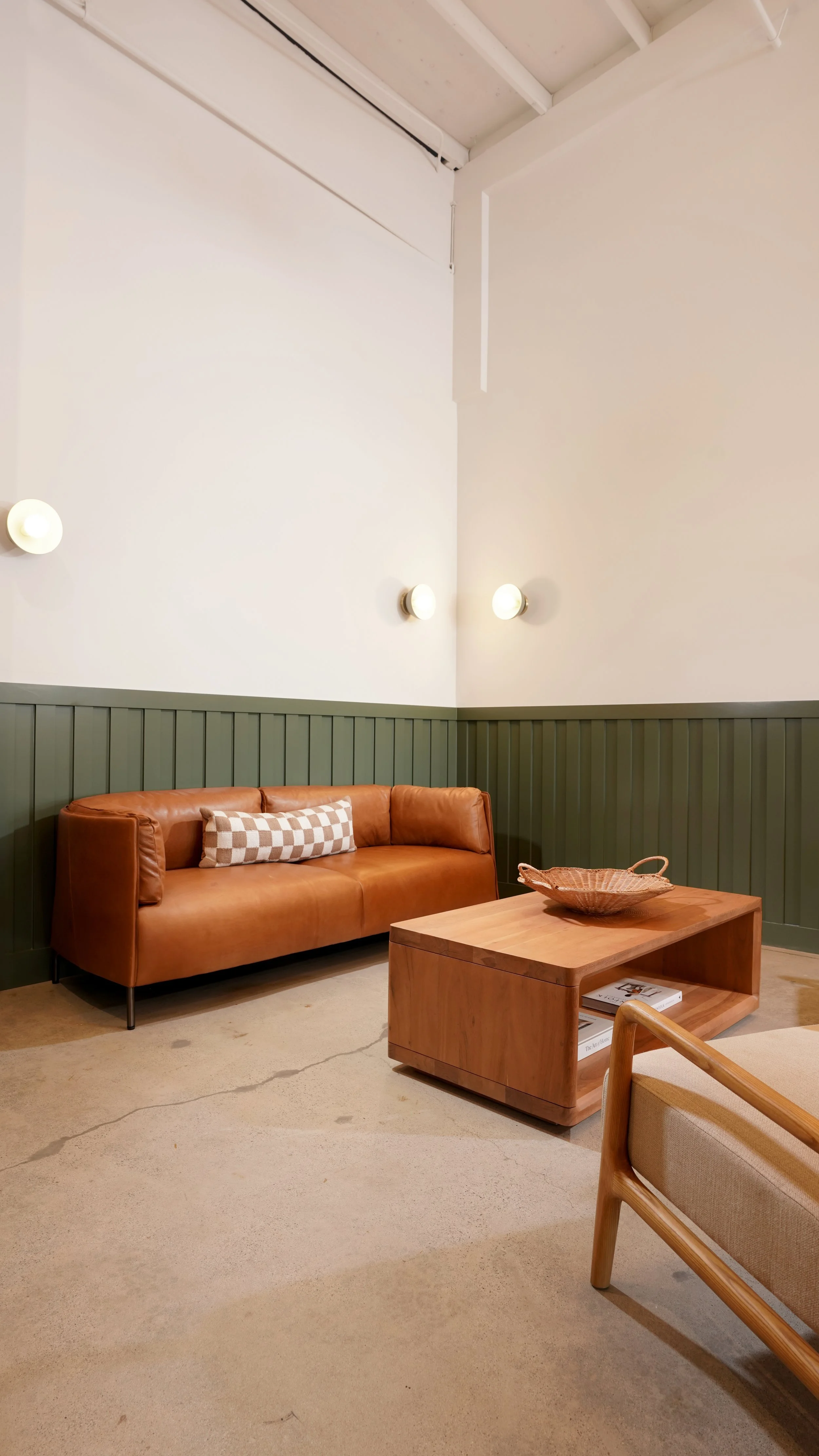 Commercial coffee shop lounge area with built-in leather bench seating, green wall paneling, wood coffee table, and soft pendant lighting.