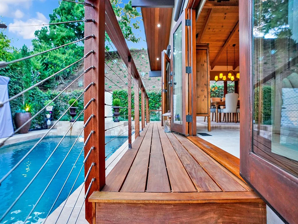 Custom wood pool deck with cable railing and folding doors connecting an Orange County backyard to the interior dining space.