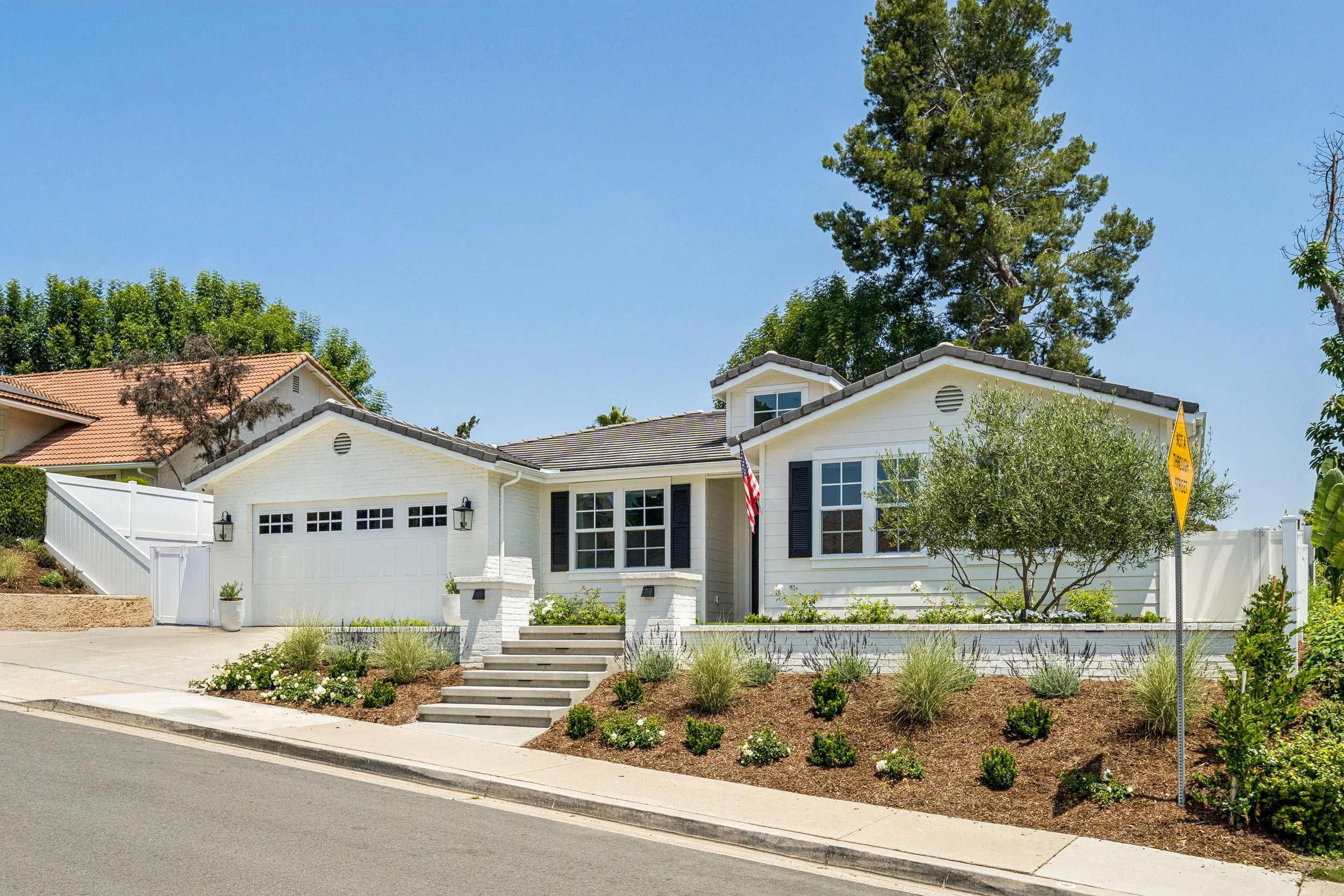 Front exterior of a renovated white coastal farmhouse-style home with fresh landscaping, white brick, black shutters, and curb appeal in Orange County.