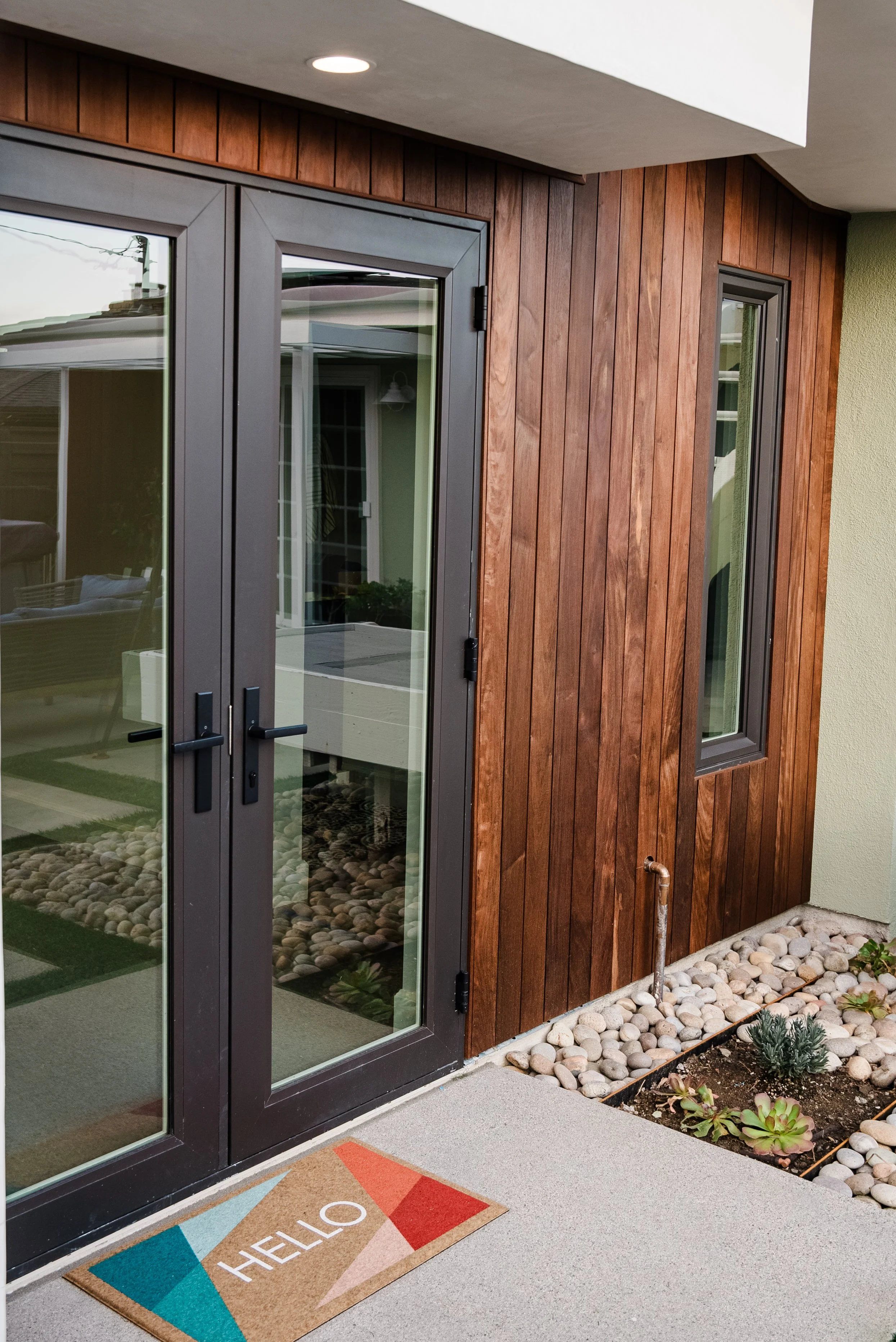 Exterior view of a modern San Clemente ADU with white stucco, vertical wood siding, black French doors, concrete pavers, and landscaped entry.