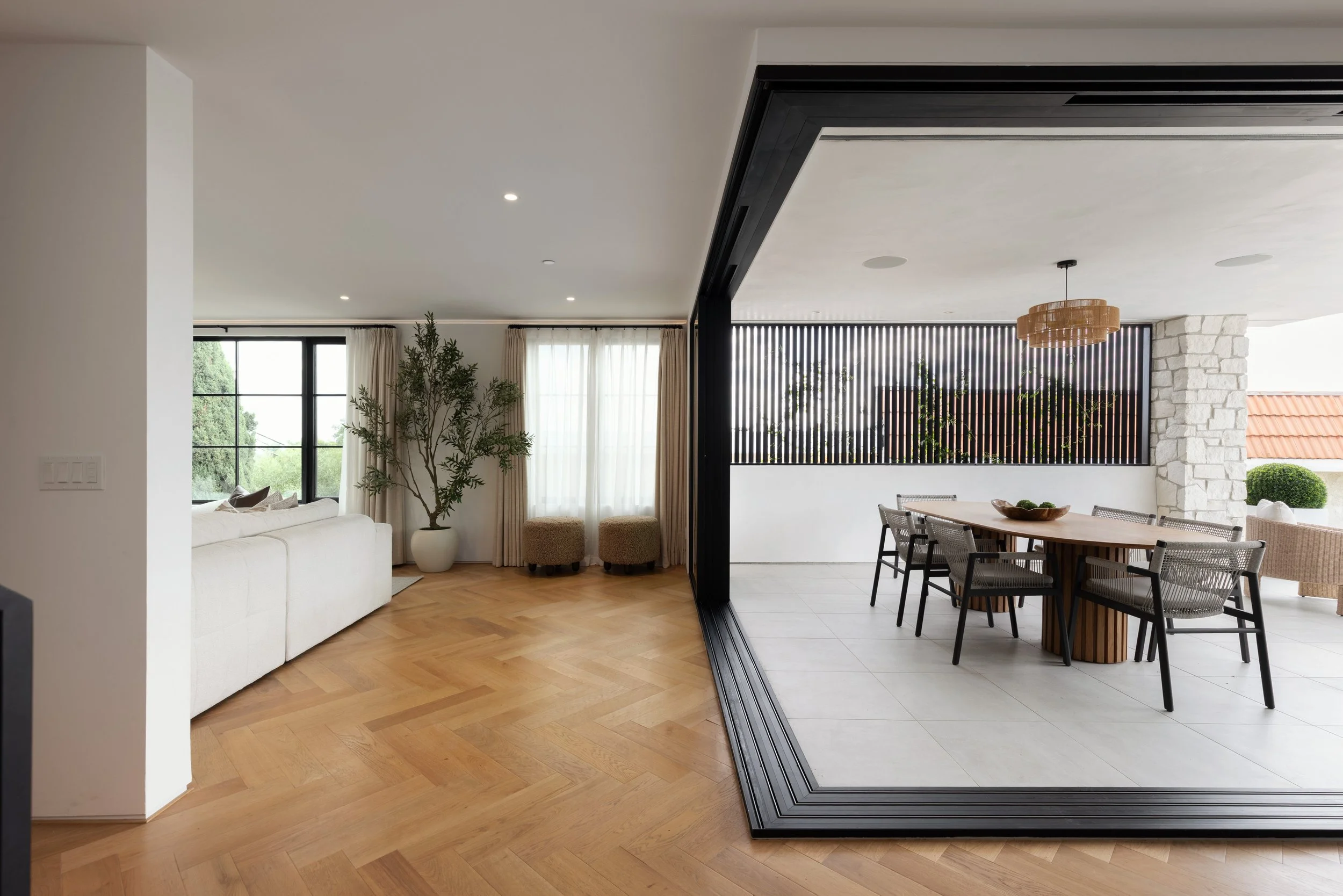 Zero-post corner bi-fold doors fully opened to create a seamless indoor-outdoor living space with herringbone wood floors and a covered patio dining area.