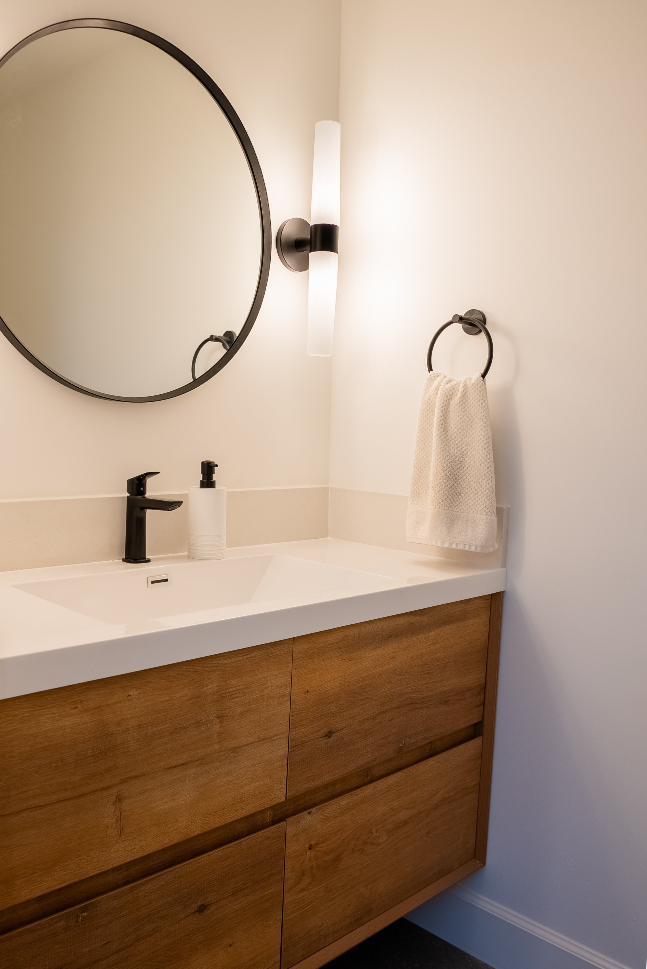 Close-up of a modern ADU bathroom vanity showing wood cabinet detail, white countertop, integrated sink edge, and hanging towel.