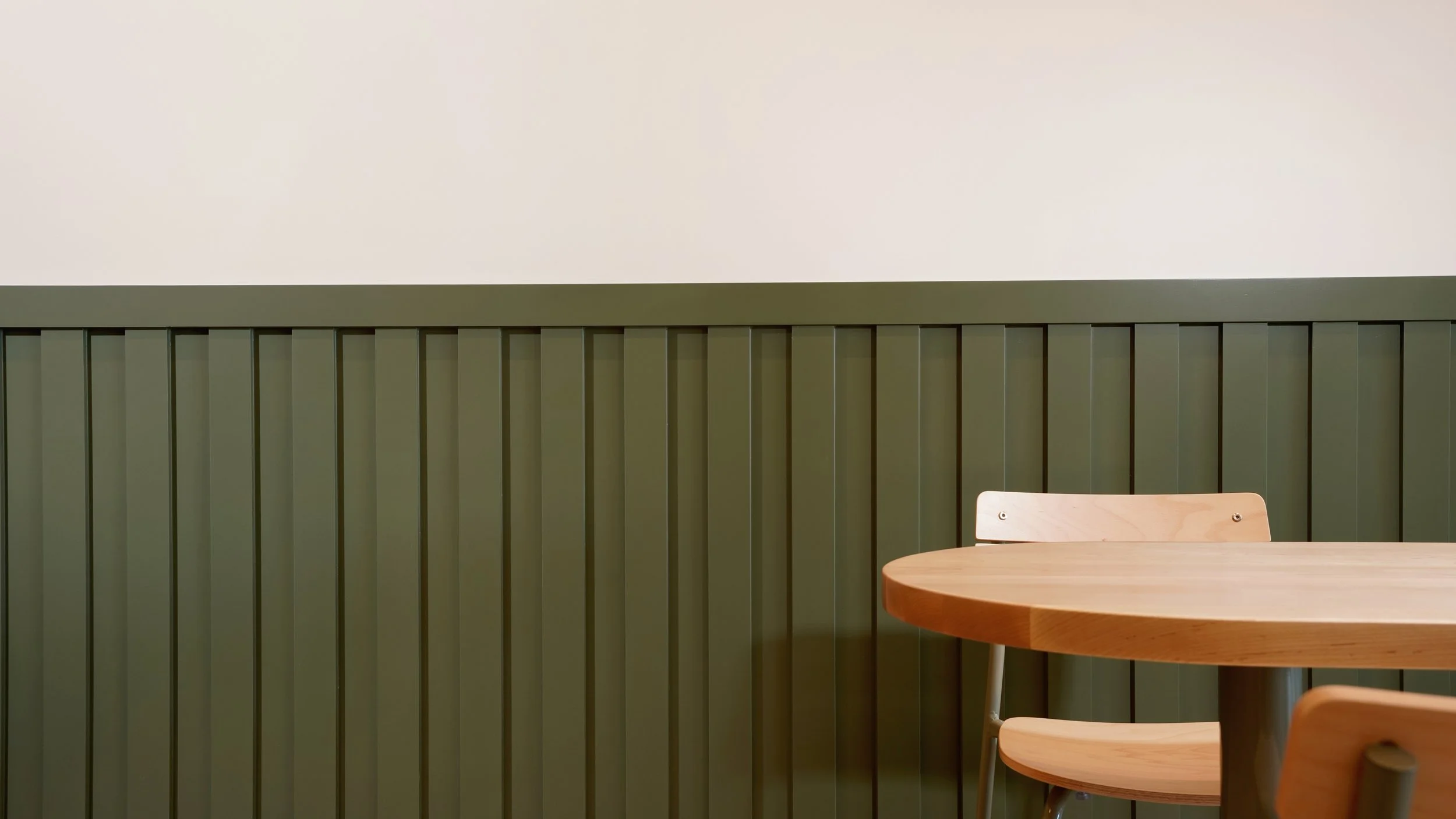 Detail of custom green wall paneling and wood cafe seating in a modern coffee shop buildout in Laguna Hills, Orange County.