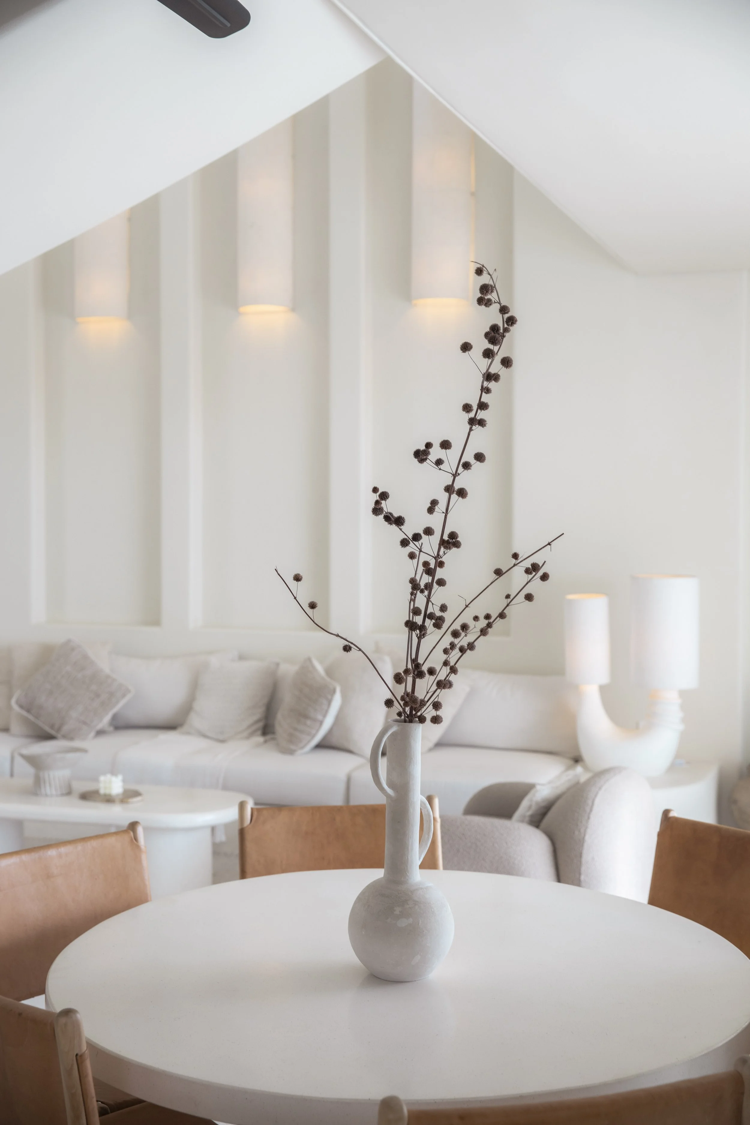 Minimalist dining area with a round table, leather dining chairs, sculptural vase, neutral furnishings, and soft architectural lighting.