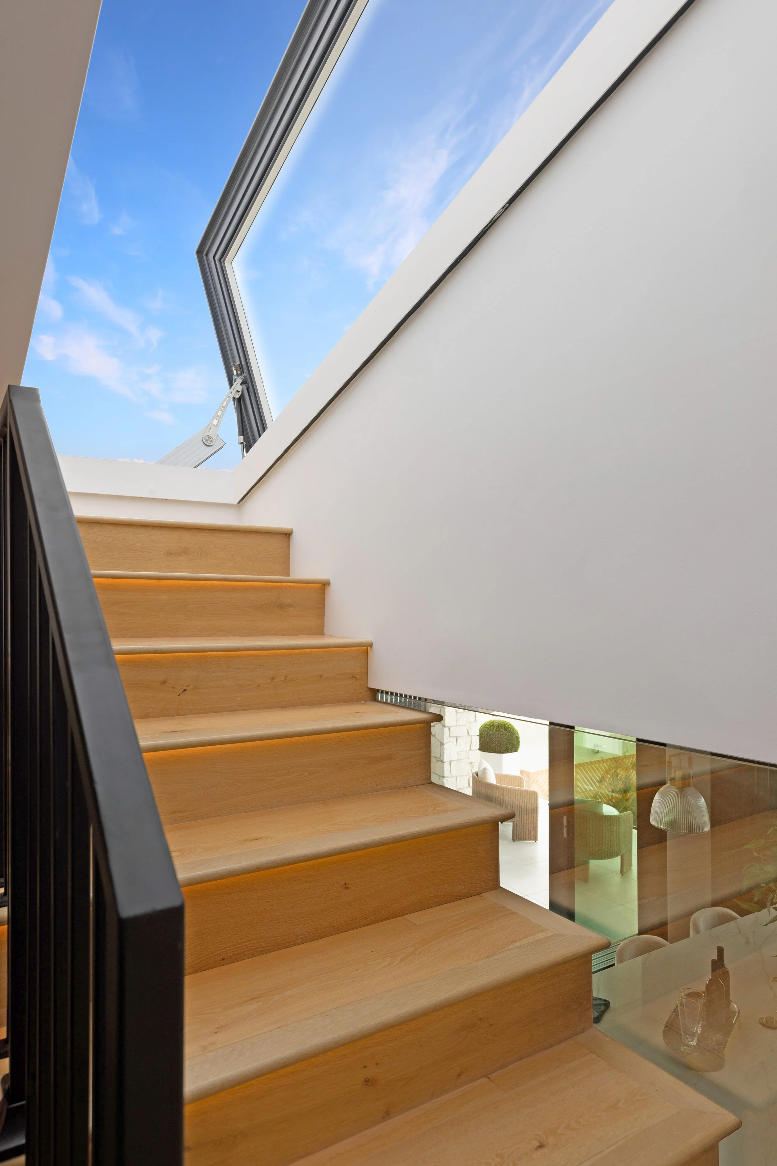 Custom wood staircase with integrated lighting and an operable skylight bringing natural light and ventilation into an Orange County home remodel.