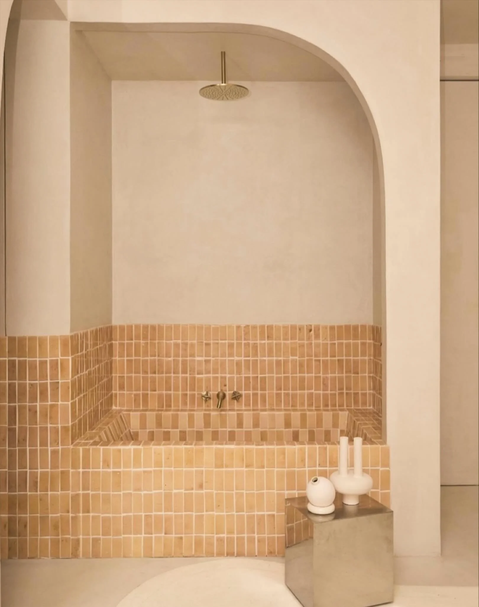 This bathroom highlights the balance between geometry and materiality. 

The custom tub is clad in handmade terracotta tiles, their irregular surface adding texture and warmth against the smooth plaster walls. 

The arched niche softens the compositi