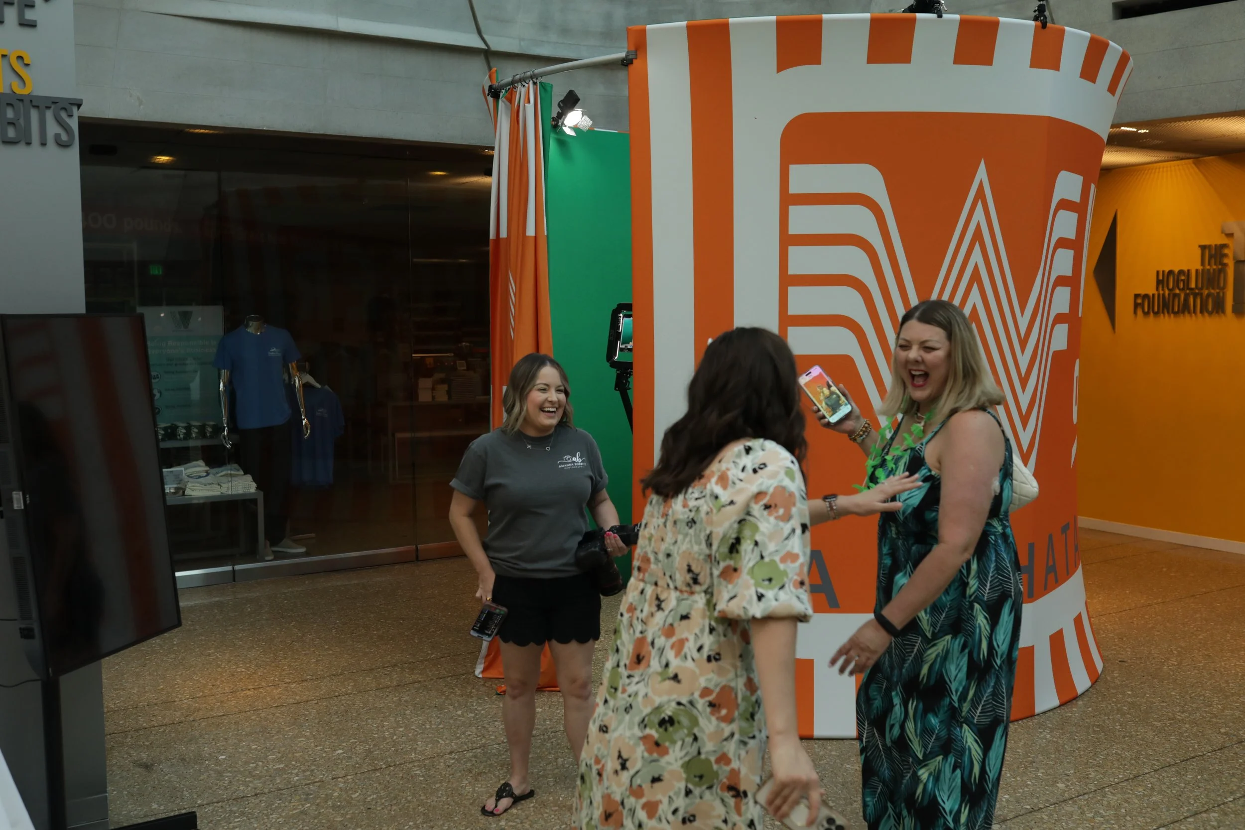 Photo of a 4x4 enclosure with a 360 photo booth setup for the 2024 McSAM Awards, with a purple archway, two vertical screens showing event graphics, and a camera on a tripod in the center.