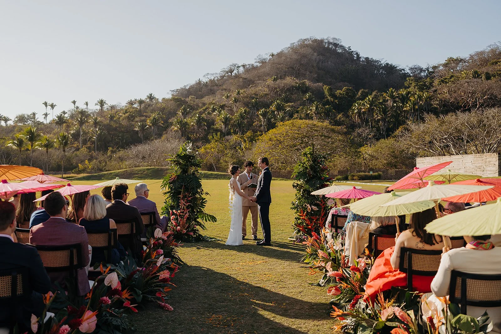 Ceremony with guests under coral parasols at Tierra Tropical Polo Club, San Pancho