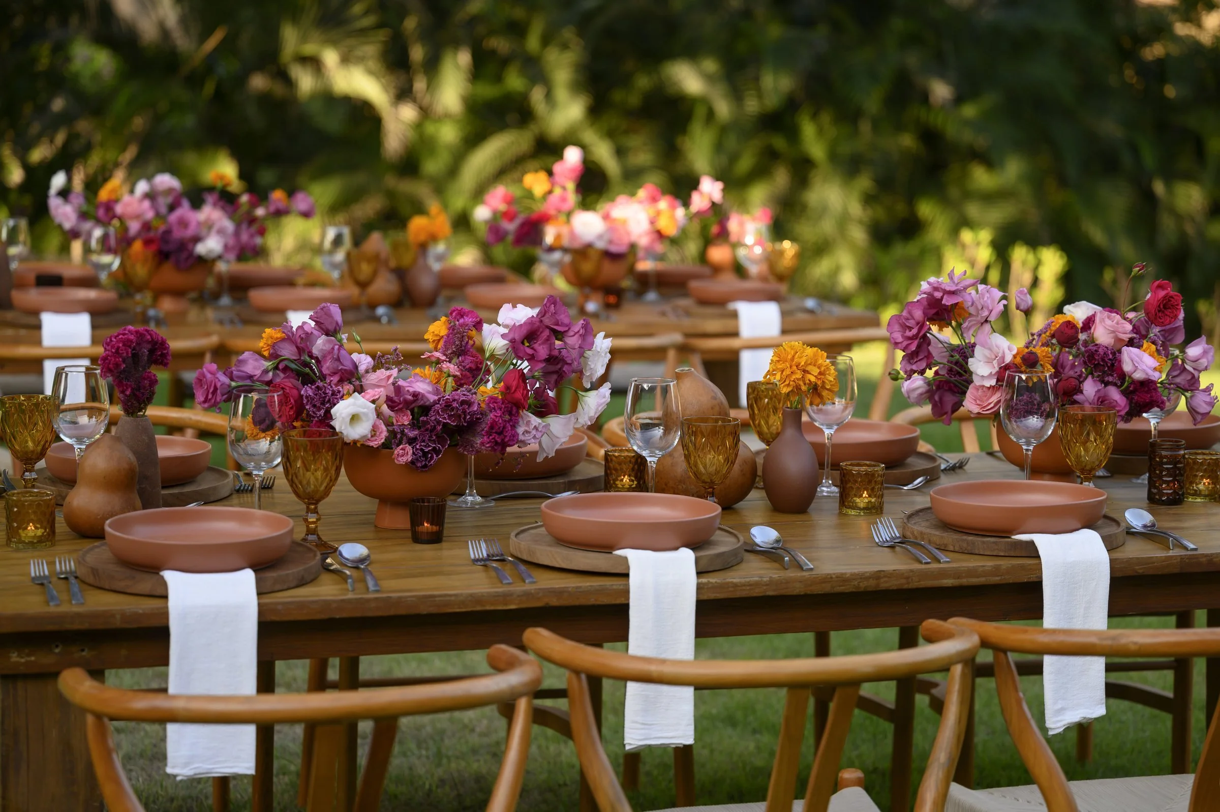 Long wood table set with terracotta plates and magenta florals at a Mexican wedding