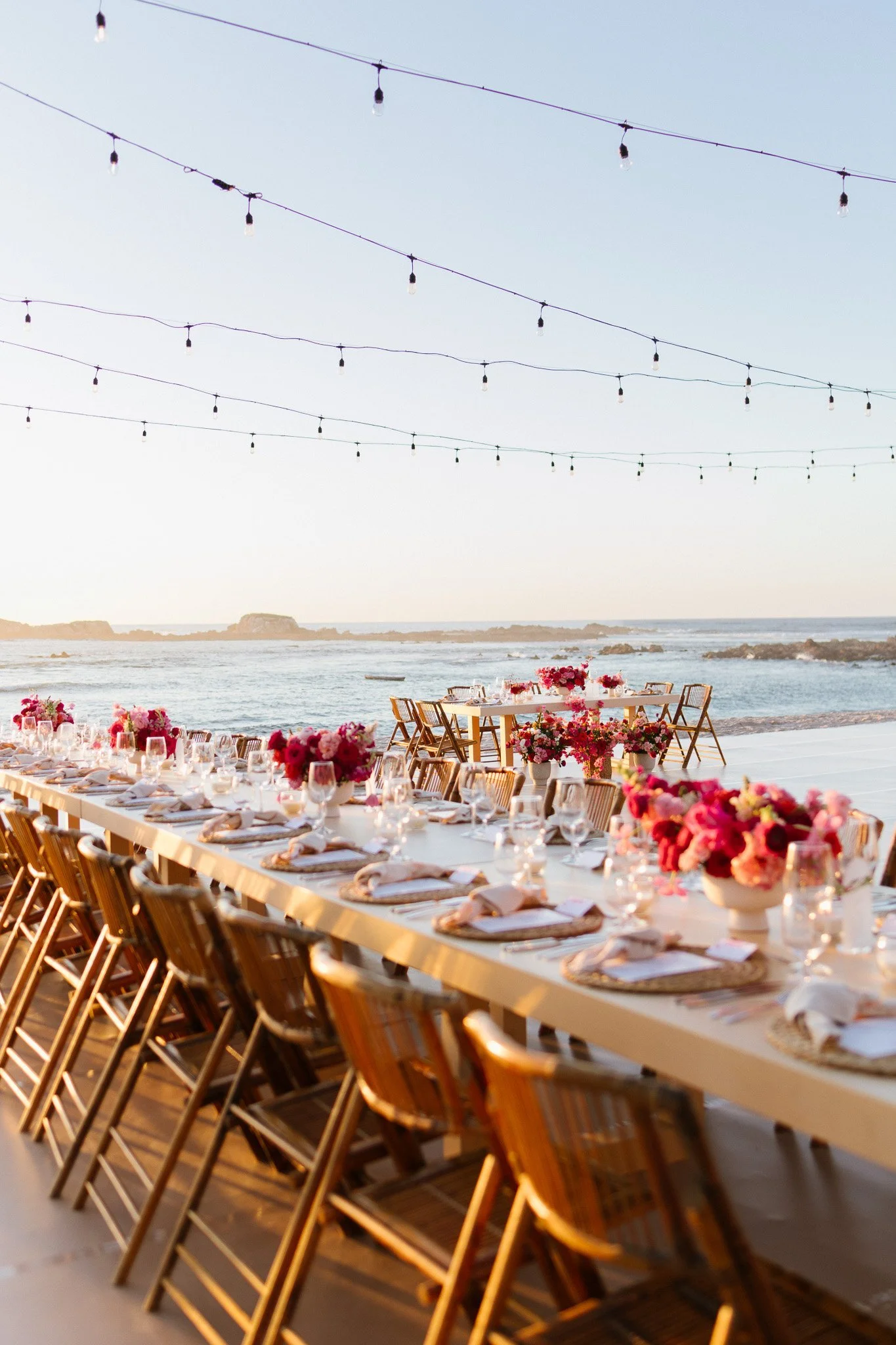 Long reception table at sunset with pink centerpieces and string lights on the beach in Punta Mita