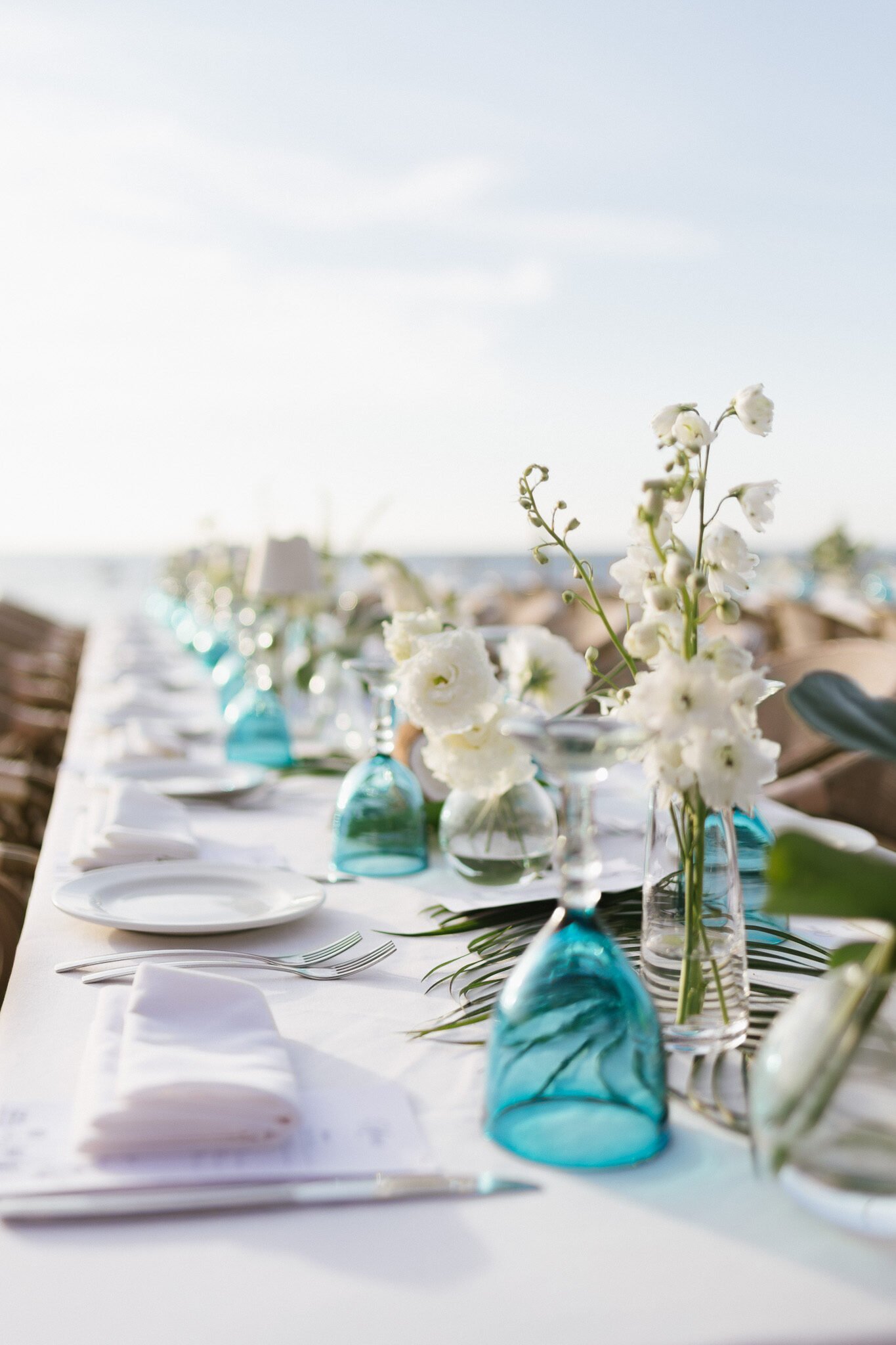 White bud vases and turquoise glass along a beachfront table at El Dorado