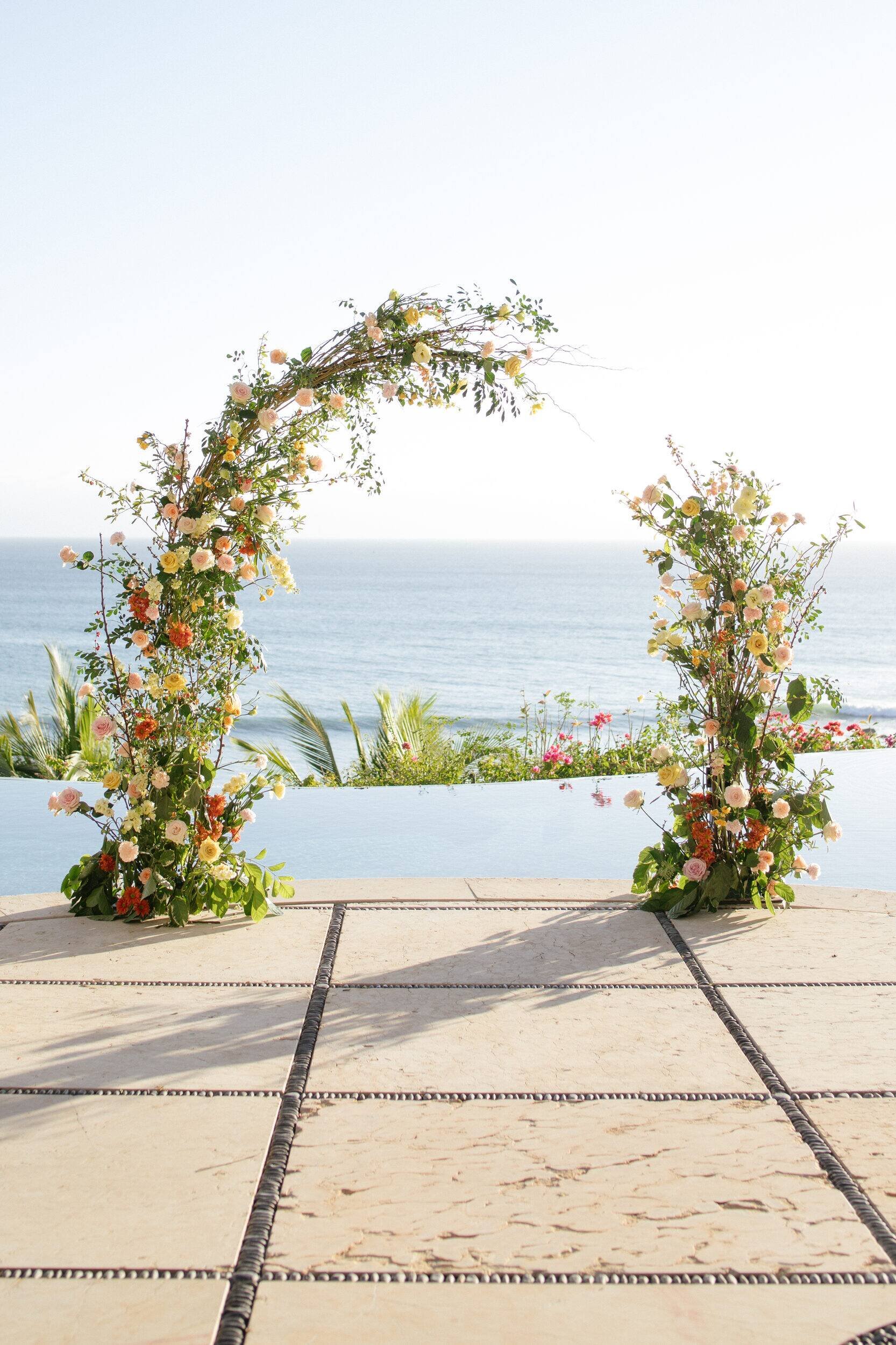 Asymmetric floral arch in coral and peach above an infinity pool, Punta de Mita