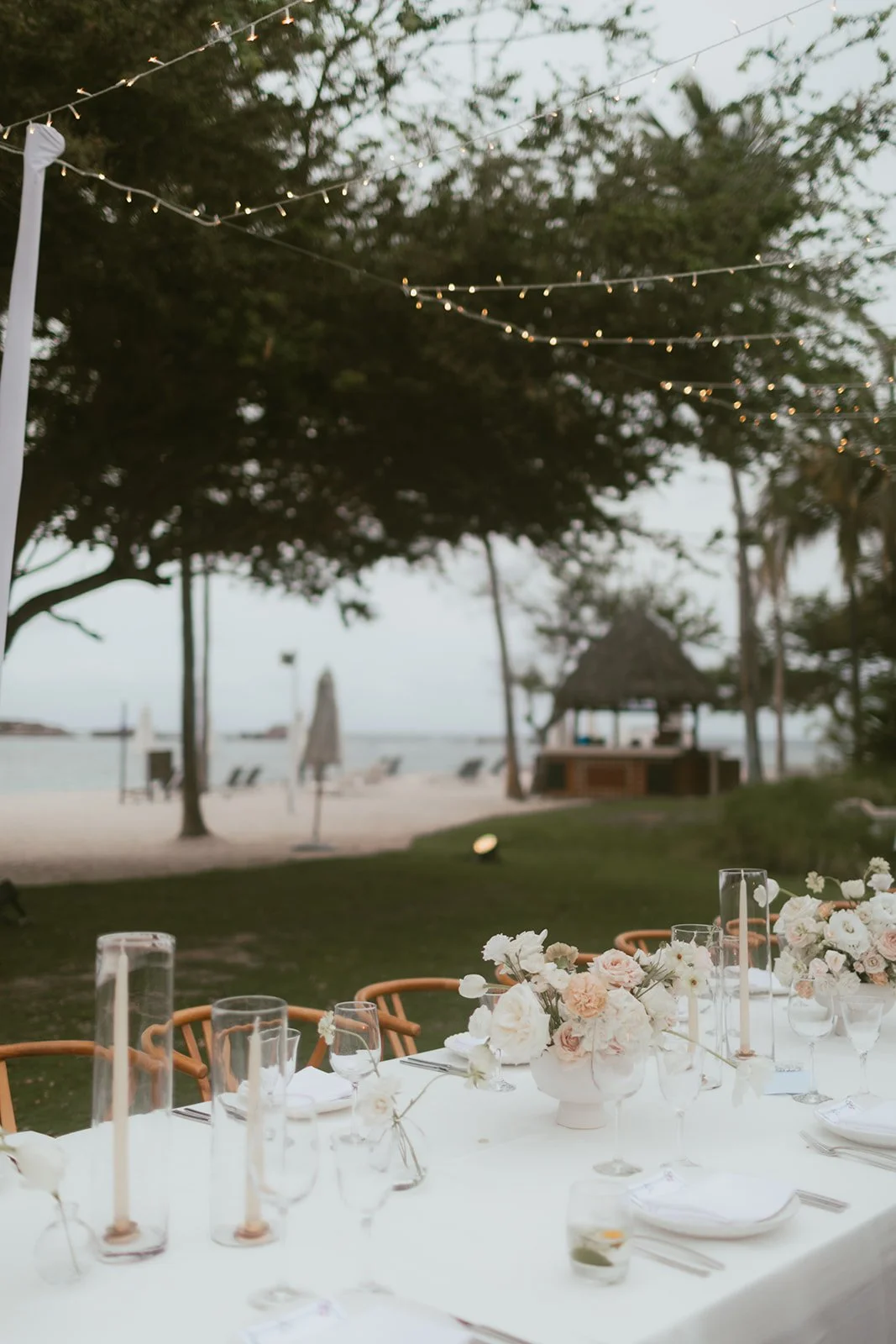 Reception table at dusk with taper candles and a blush and cream centerpiece, beach behind