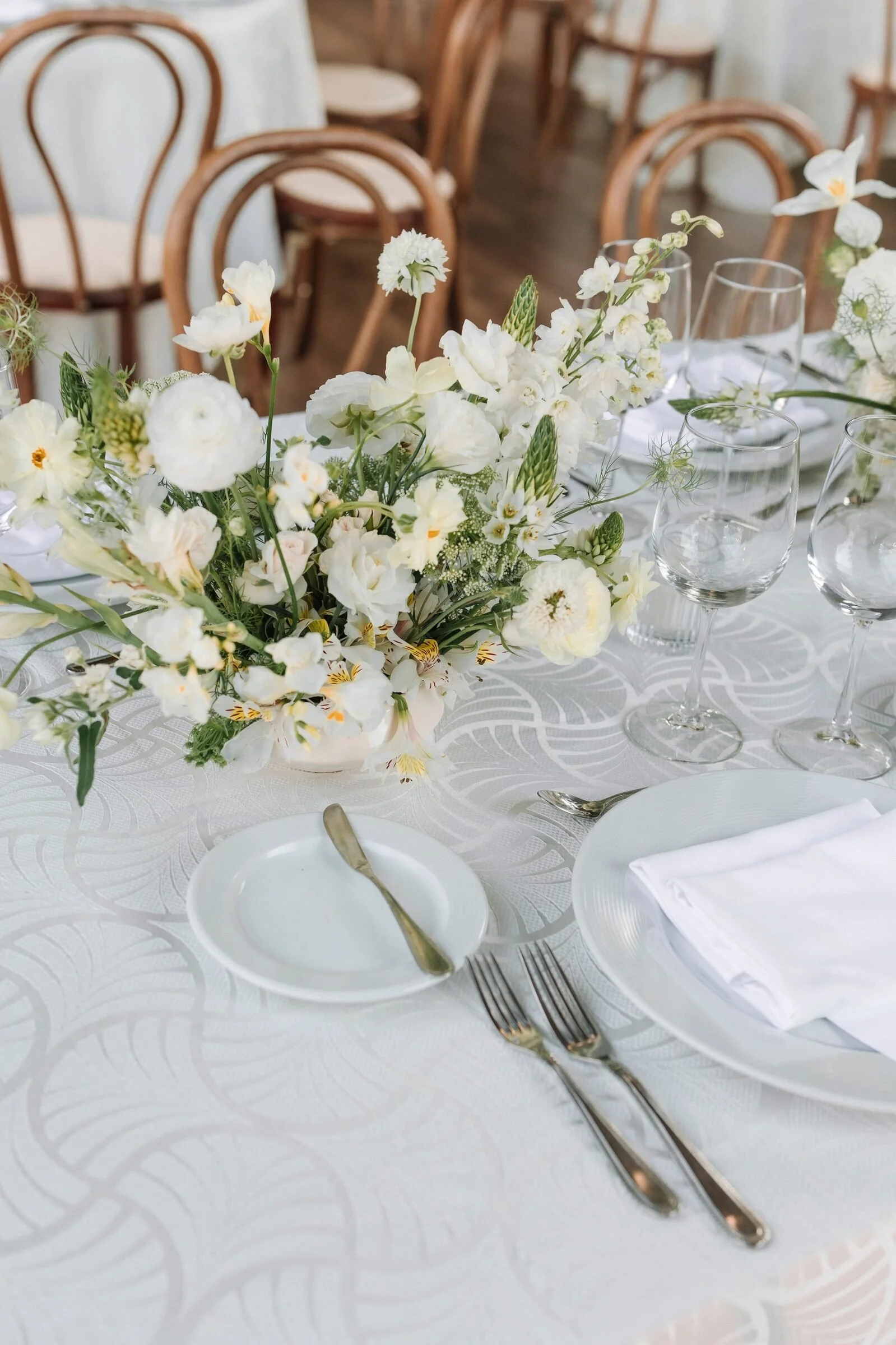 Low centerpiece of ranunculus, freesia and alstroemeria beside a white place setting at Garza Blanca