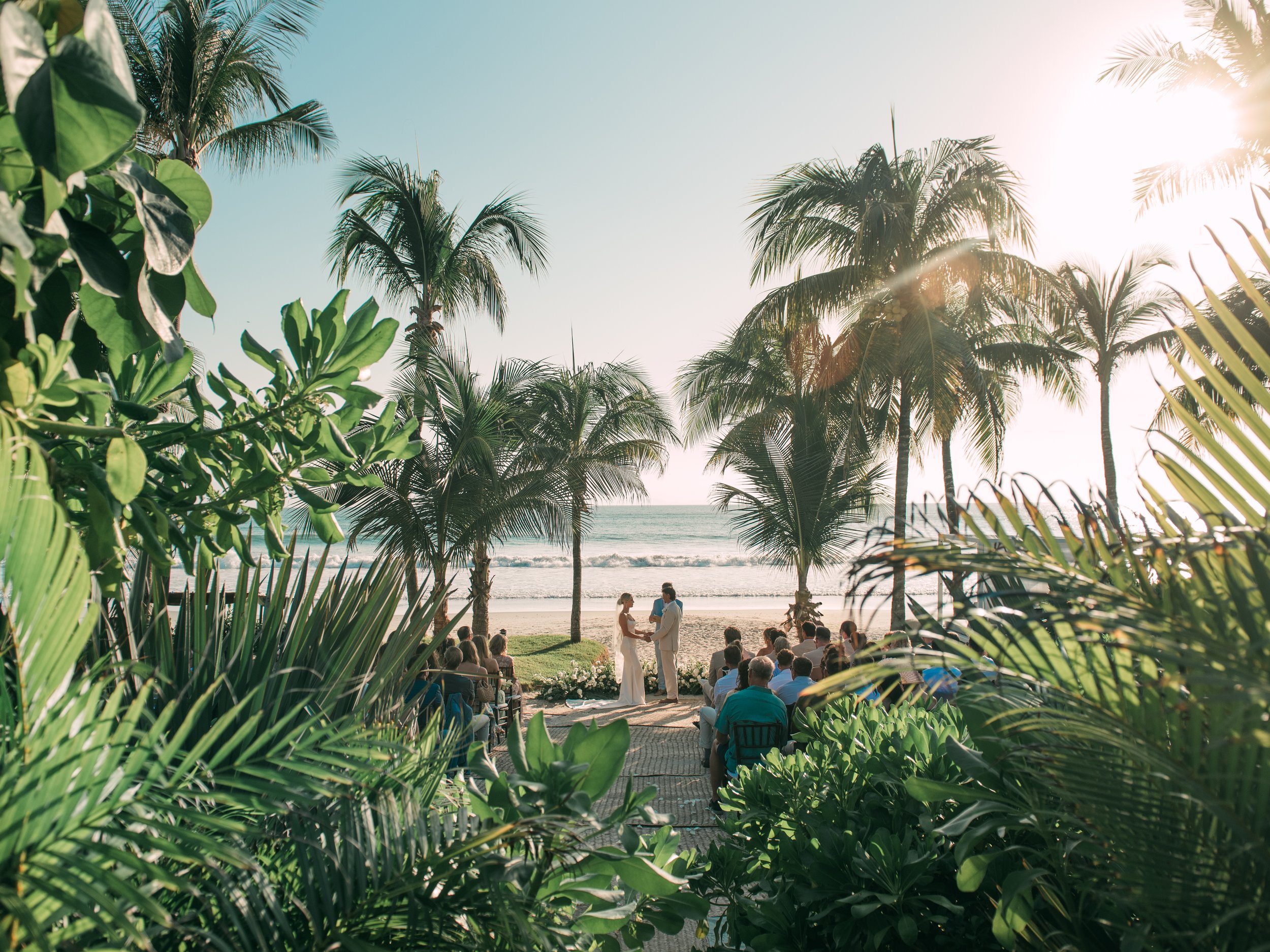 Beach ceremony seen through tropical foliage at W Punta de Mita